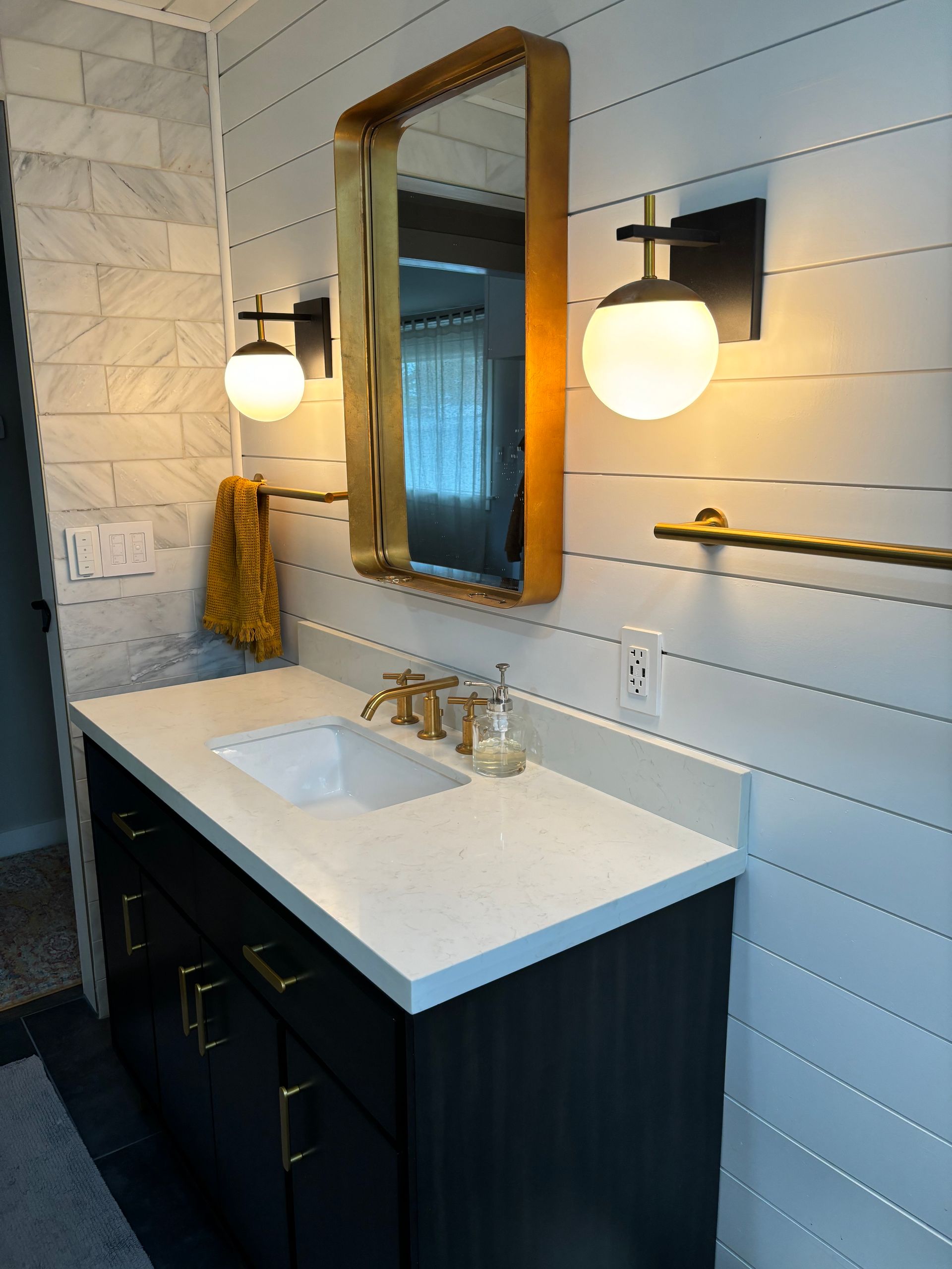Modern bathroom vanity with white sink, dark cabinet, mirror, and globe lights in a tiled room