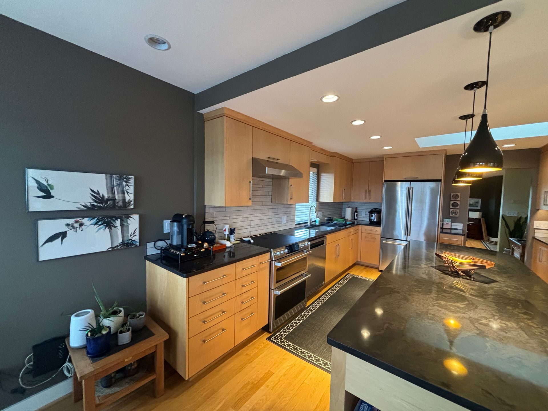 Modern kitchen with wood cabinets, stainless steel appliances, black countertops, and pendant lights over an island.