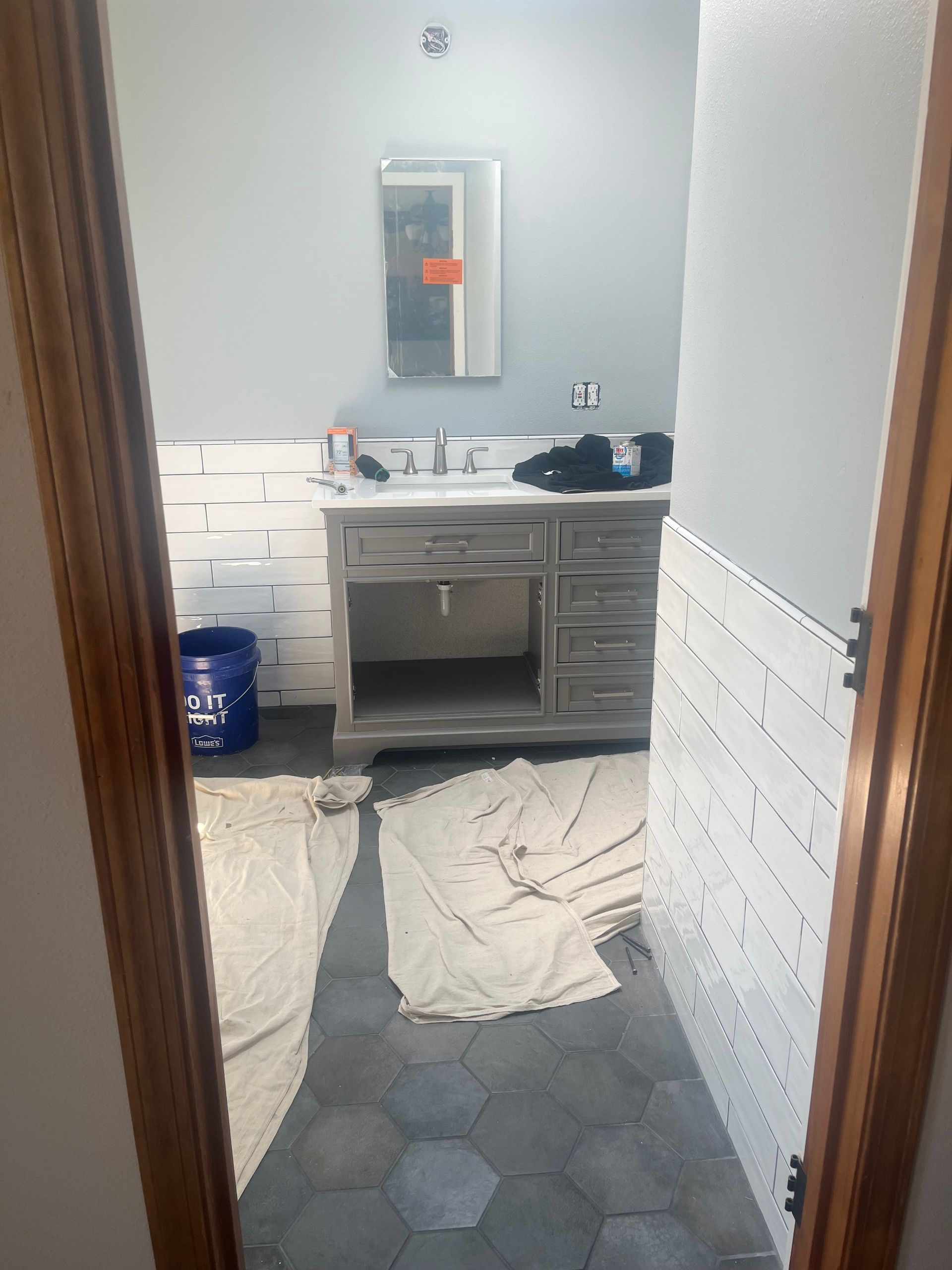 Small bathroom under renovation with sink, mirror, blue tile floor, and plastic-covered walls.