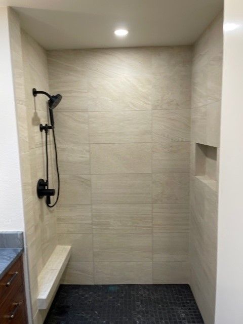 Modern tiled walk-in shower with black fixtures, recessed shelf, and ceiling light