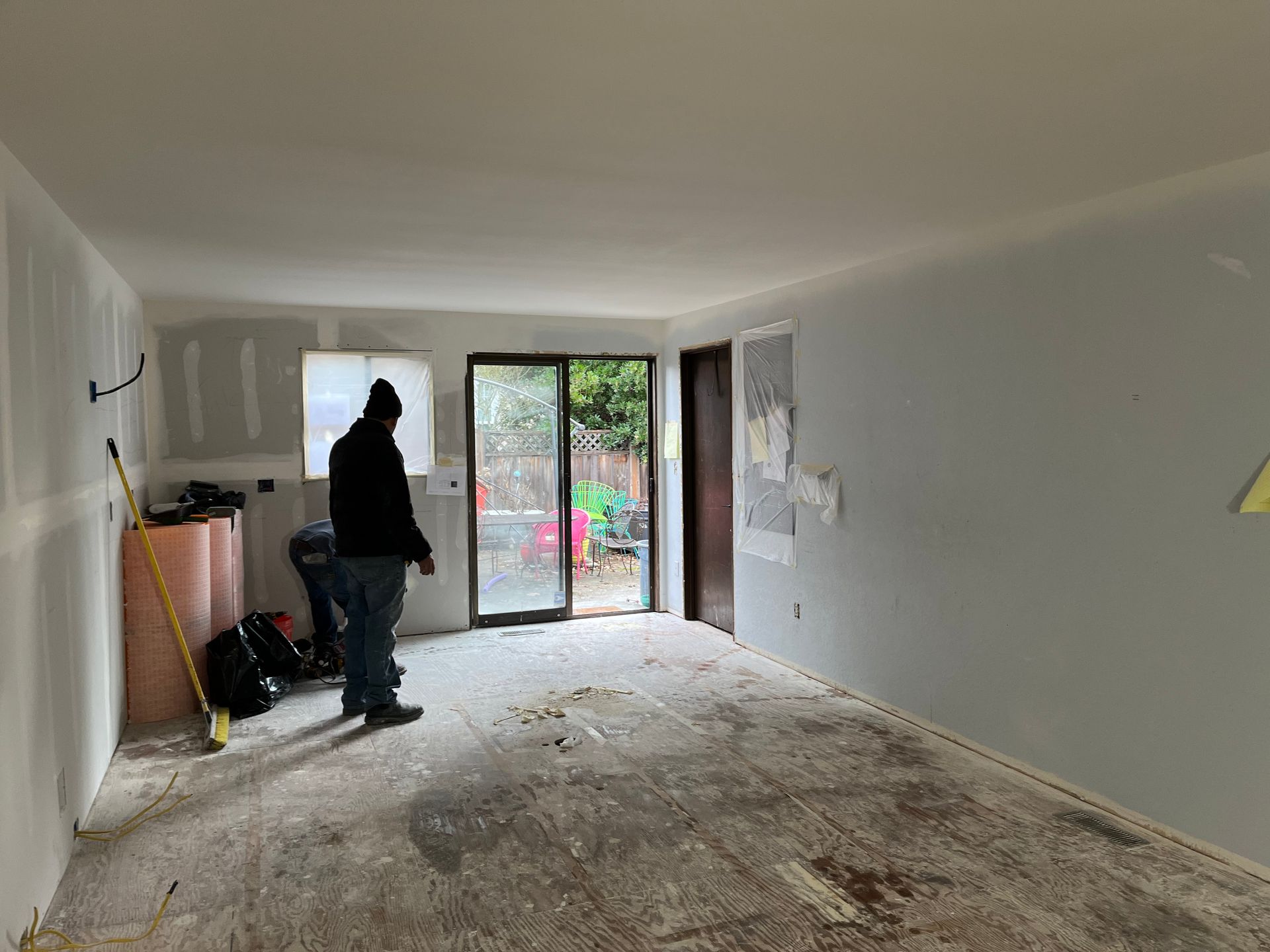 Person cleaning a dusty, unfinished room with tools near a sliding glass door