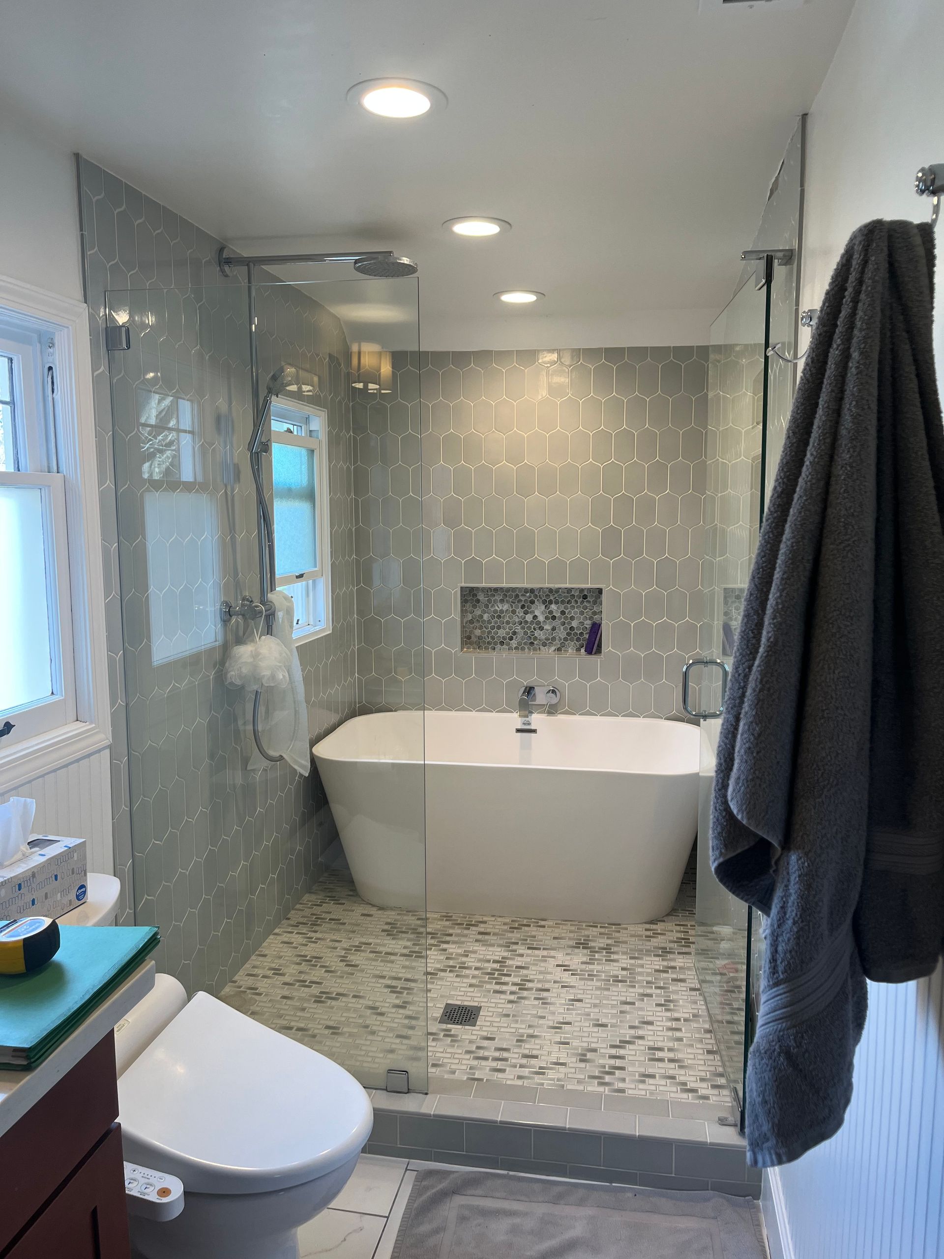 Modern gray-tiled bathroom with freestanding tub, shower, toilet, and dark towels
