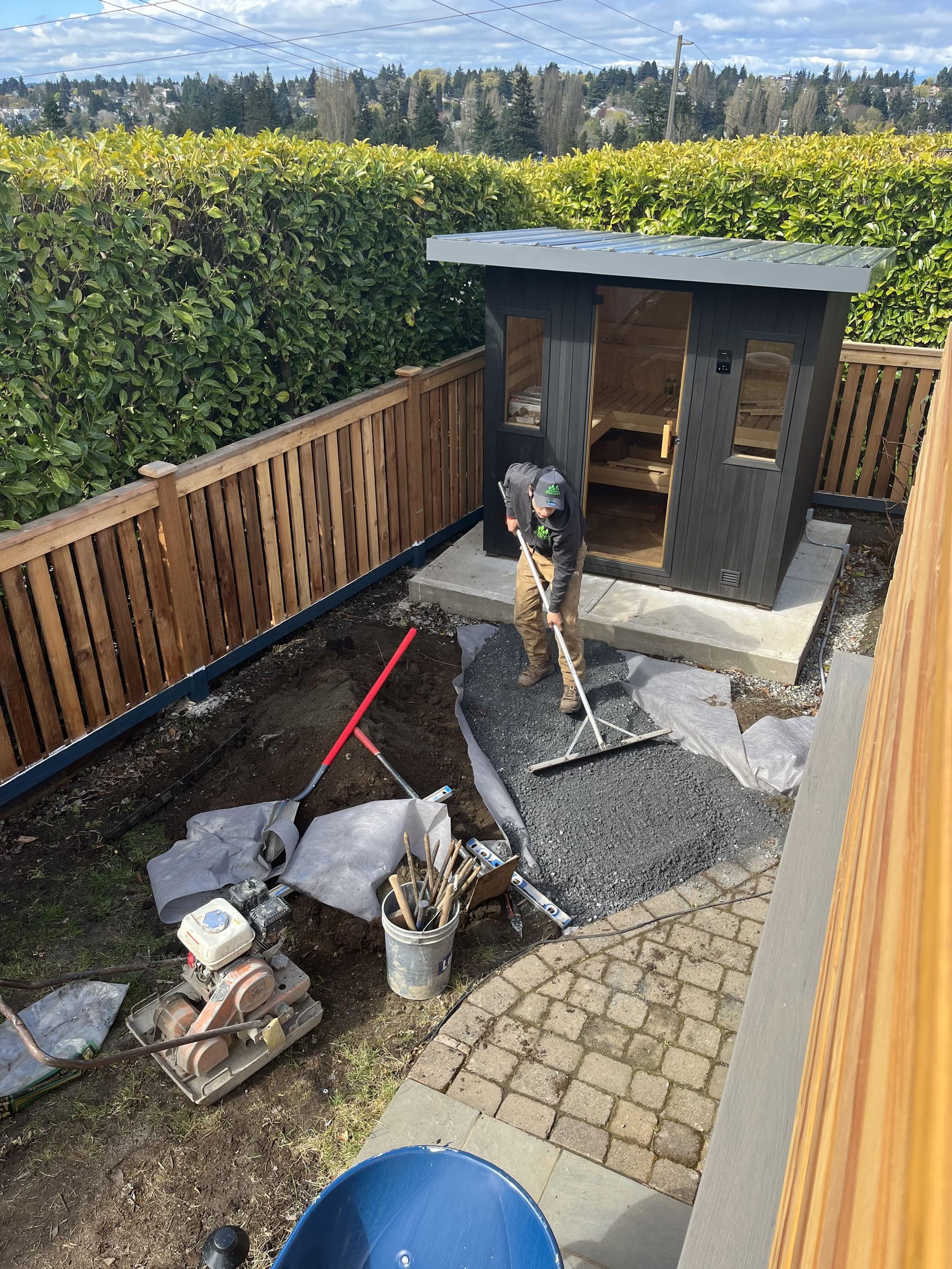 Backyard patio with a small shed, gravel area, fence, and garden tools on a sunny day
