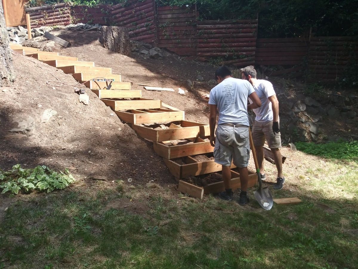 Two workers building wooden steps into a dirt slope in a backyard