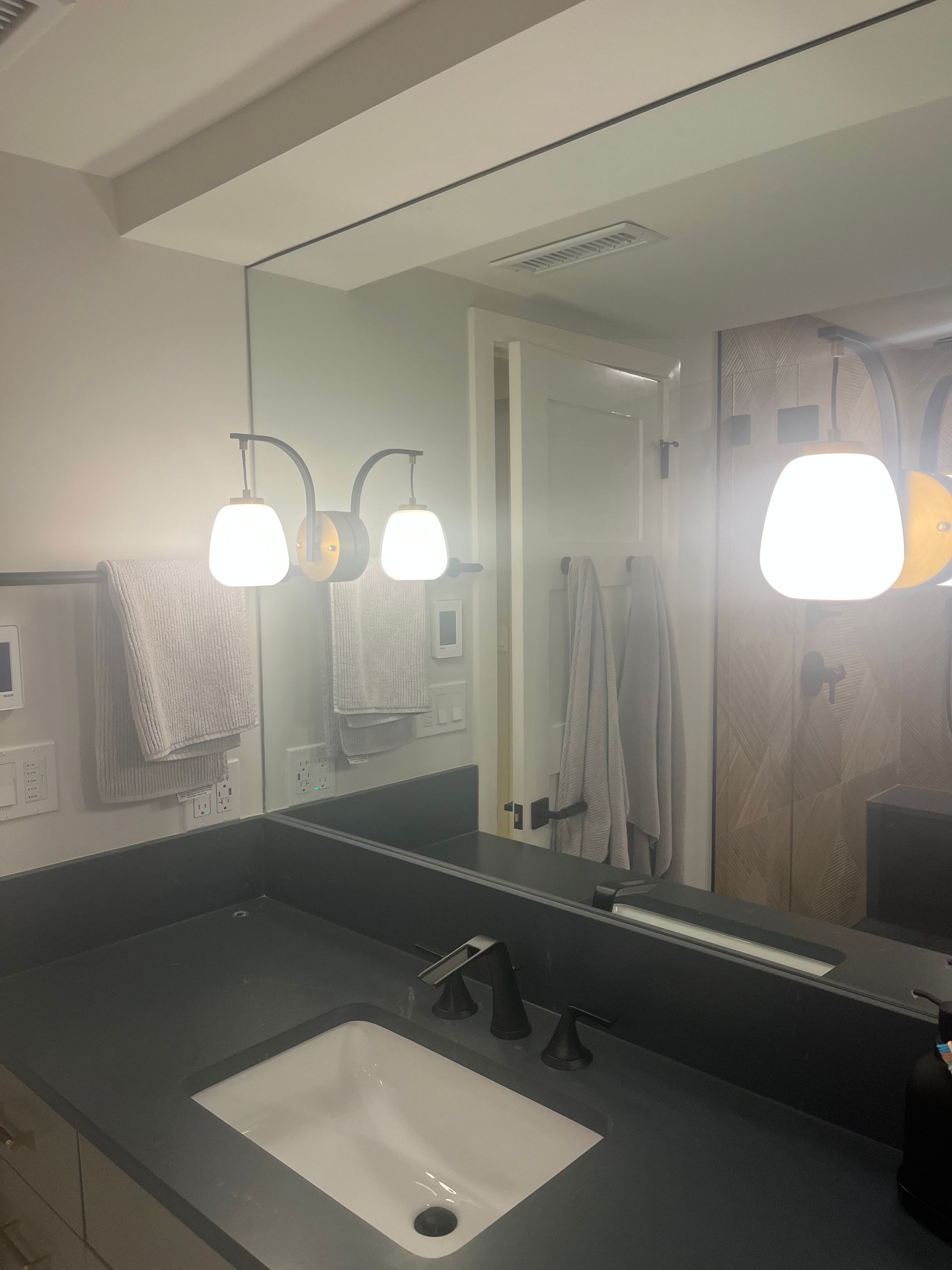 Bathroom vanity with white sink, black countertop, large mirror, and two lit pendant lights.