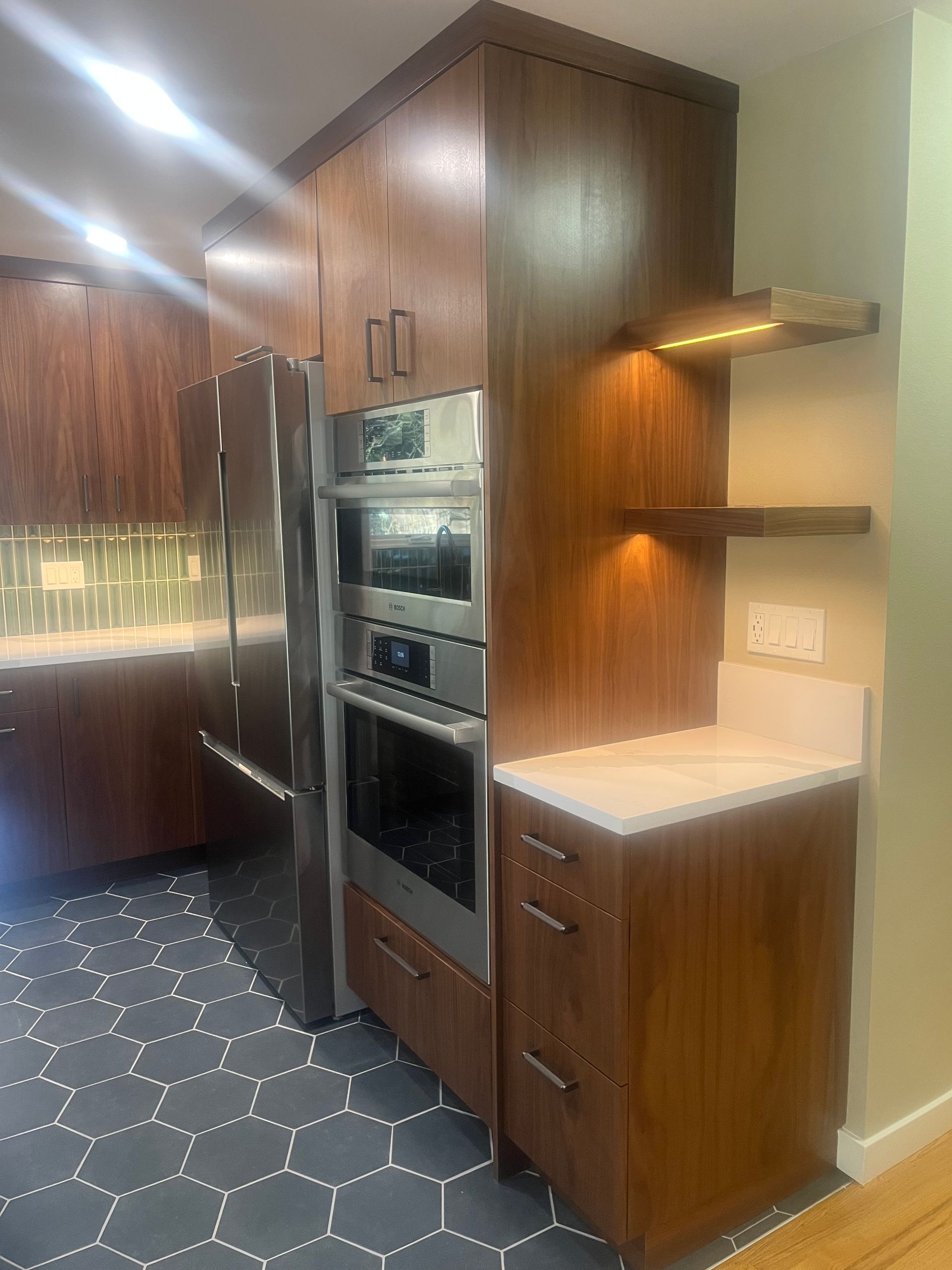 Modern kitchen with wood cabinets, built-in oven, white countertop, and dark hexagon-tile floor.
