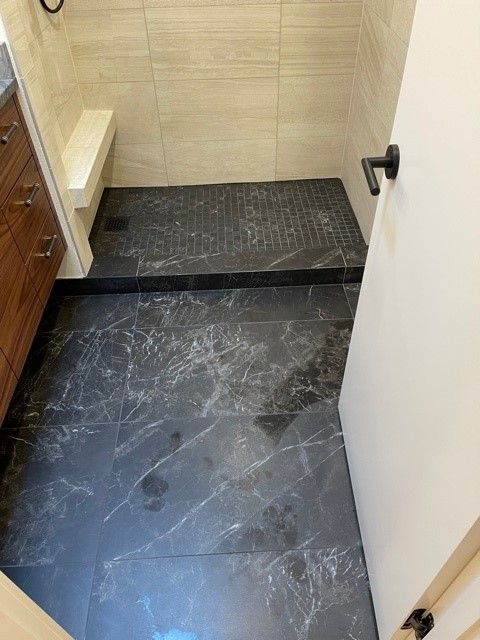 Small bathroom with black stone floor, beige tiled step, and partially open white door.