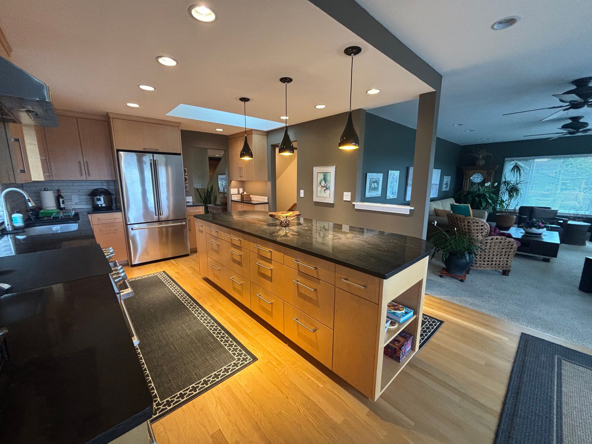 Modern kitchen with island, stainless steel fridge, and open view into a living room.