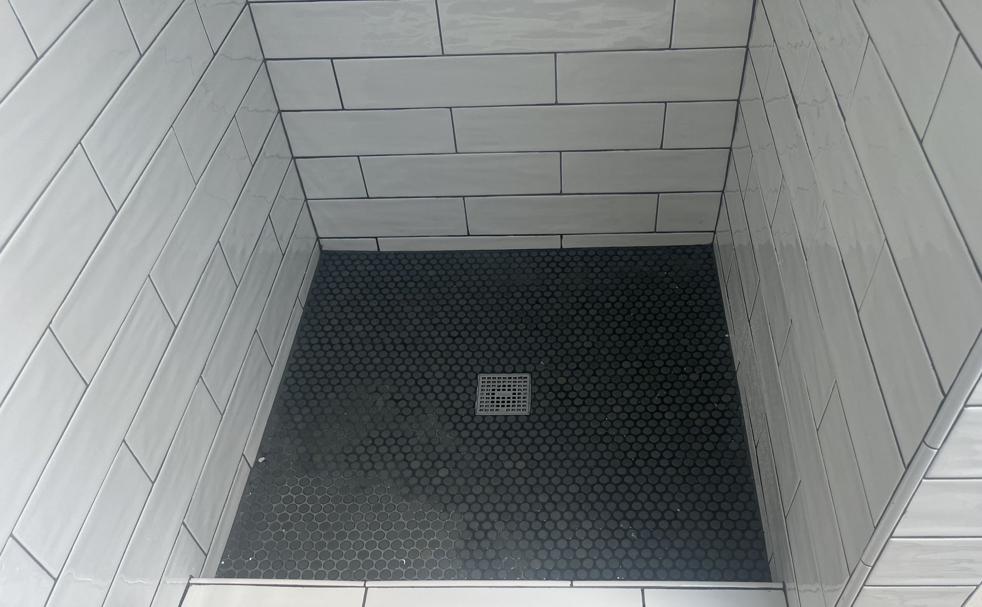 Empty tiled shower stall with black drain floor and white brick walls