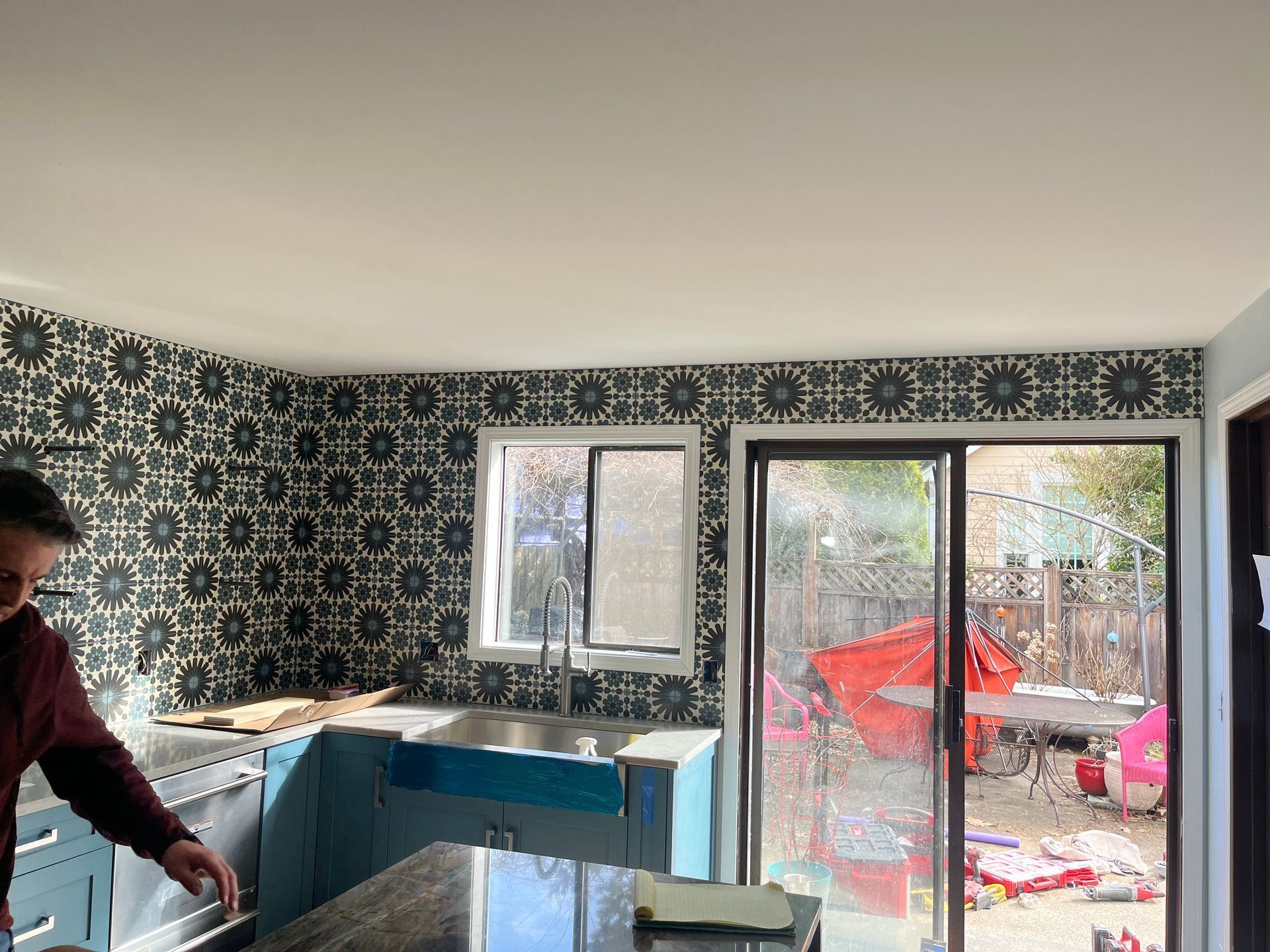 Kitchen with black-and-white patterned wallpaper, blue cabinets, and sliding glass doors to a patio.