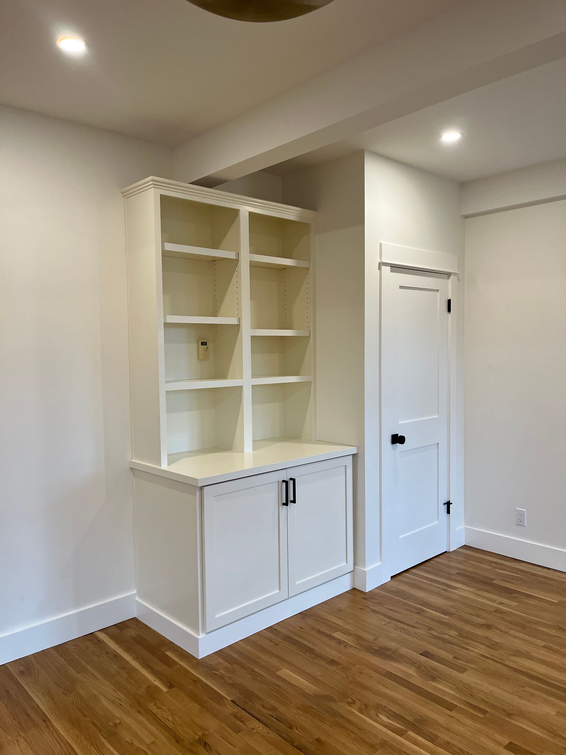 Empty white room with built-in shelving, cabinet, closet door, and hardwood floor.
