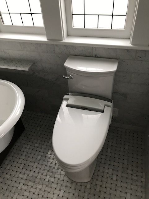Modern toilet with bidet seat in a tiled bathroom beside a sink and windowed wall
