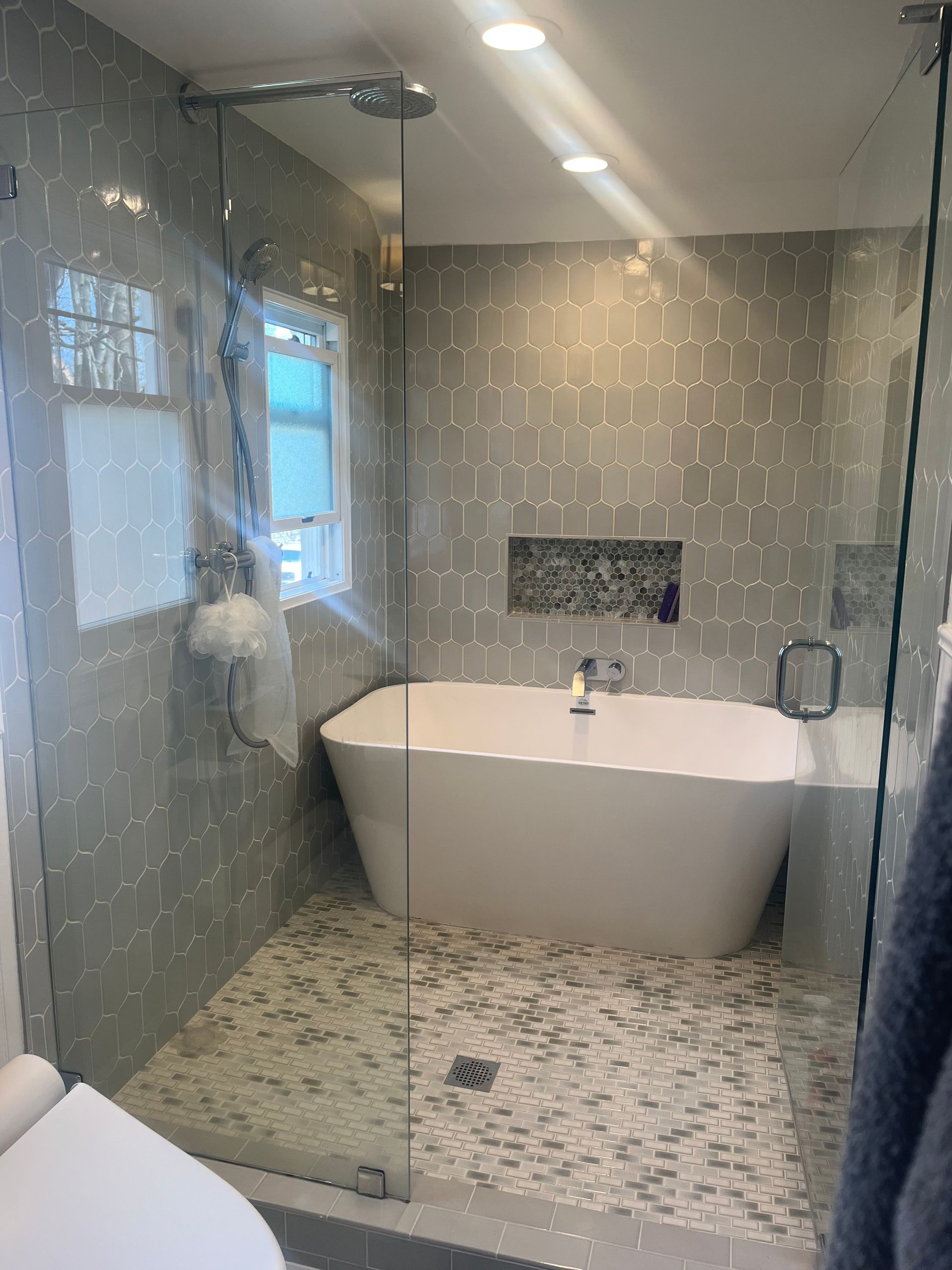 Modern bathroom with glass shower, freestanding tub, and mosaic tile floor and walls