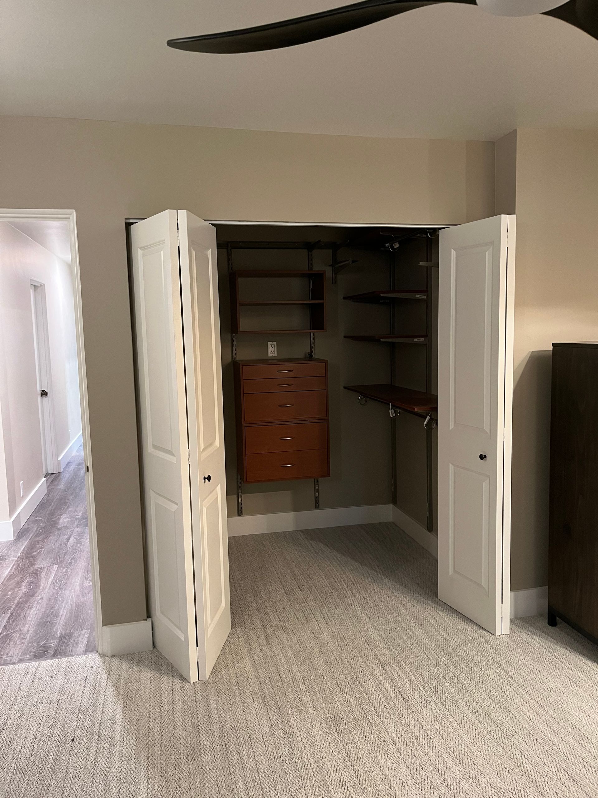 Open closet with white double doors, shelves, and a wood drawer unit in a carpeted room.