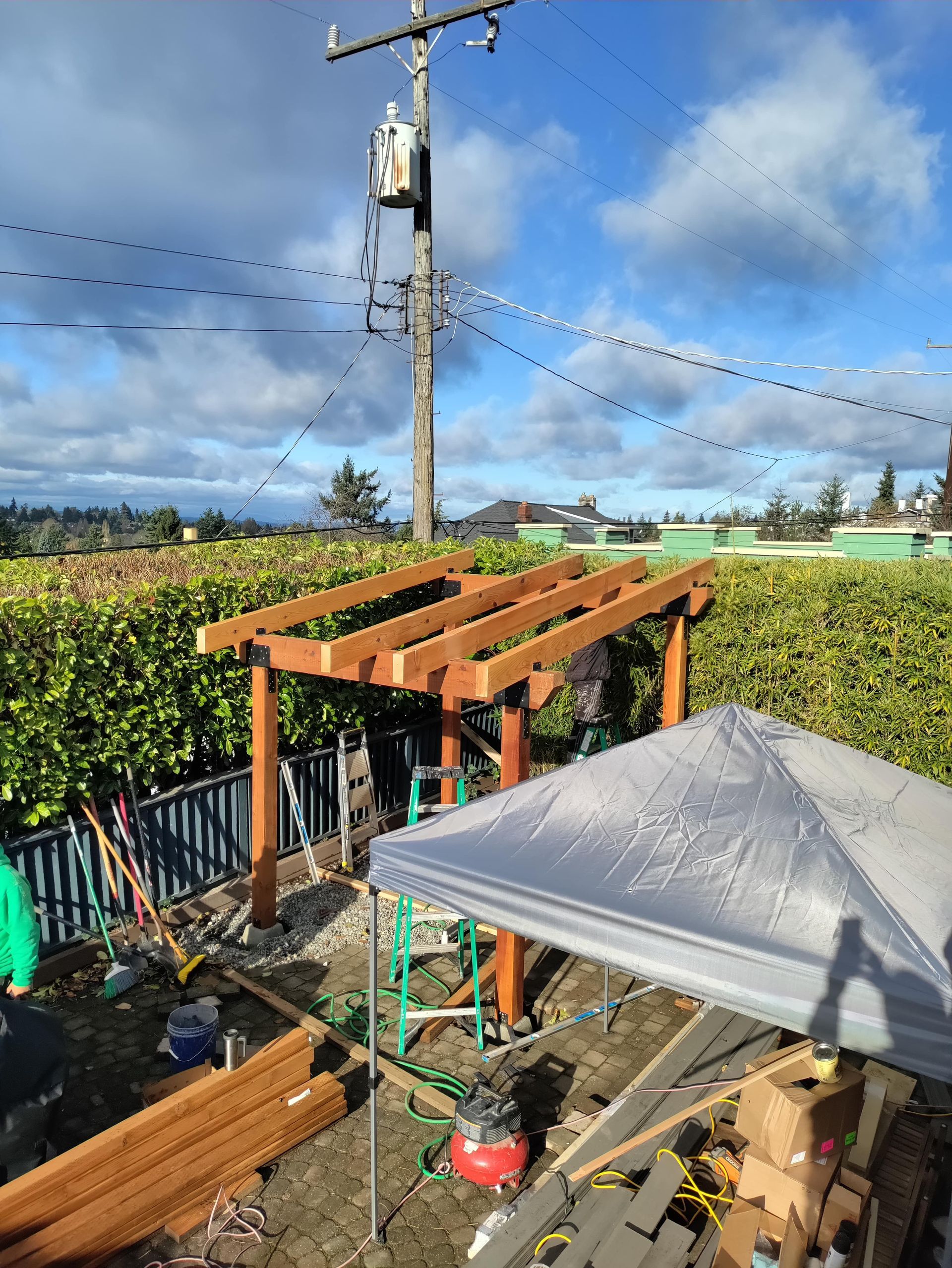 Backyard garden with wooden pergola, patio umbrella, power pole, and string lights under a blue sky