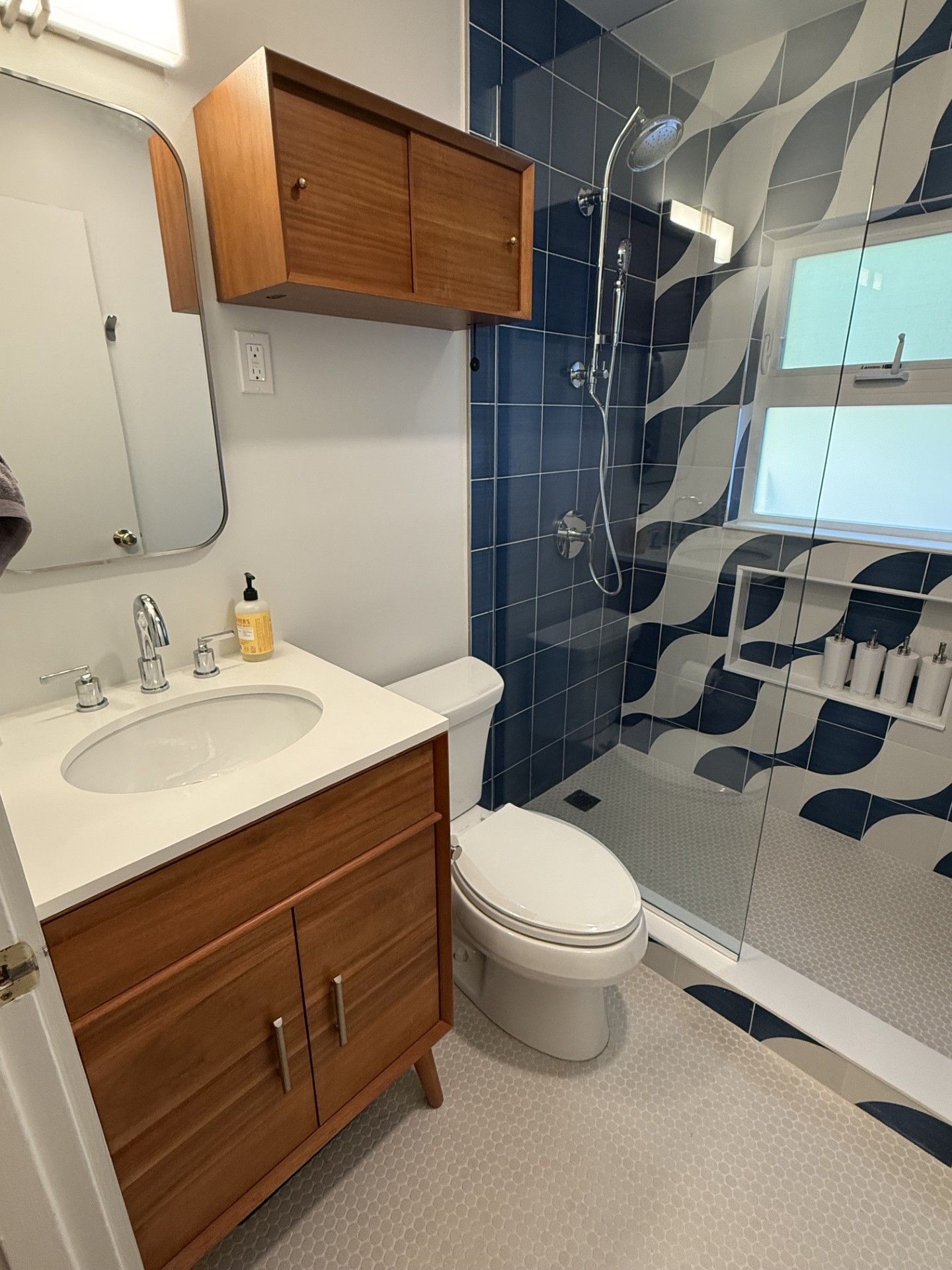 Compact bathroom with wood vanity, white sink and toilet, and blue tiled shower wall.