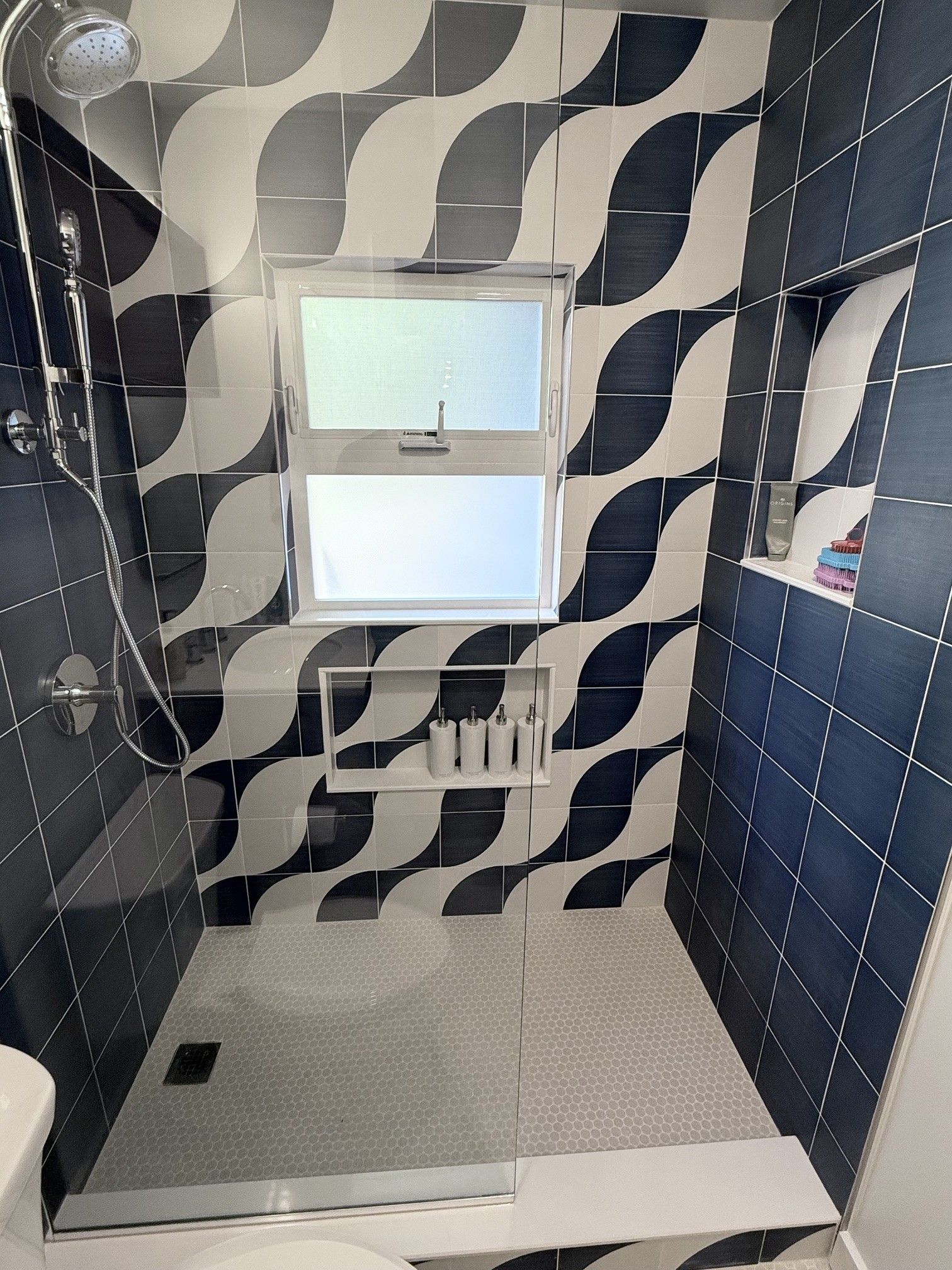 Bathroom with blue-and-white tiled walls, a small window, and a shower area with a drain.