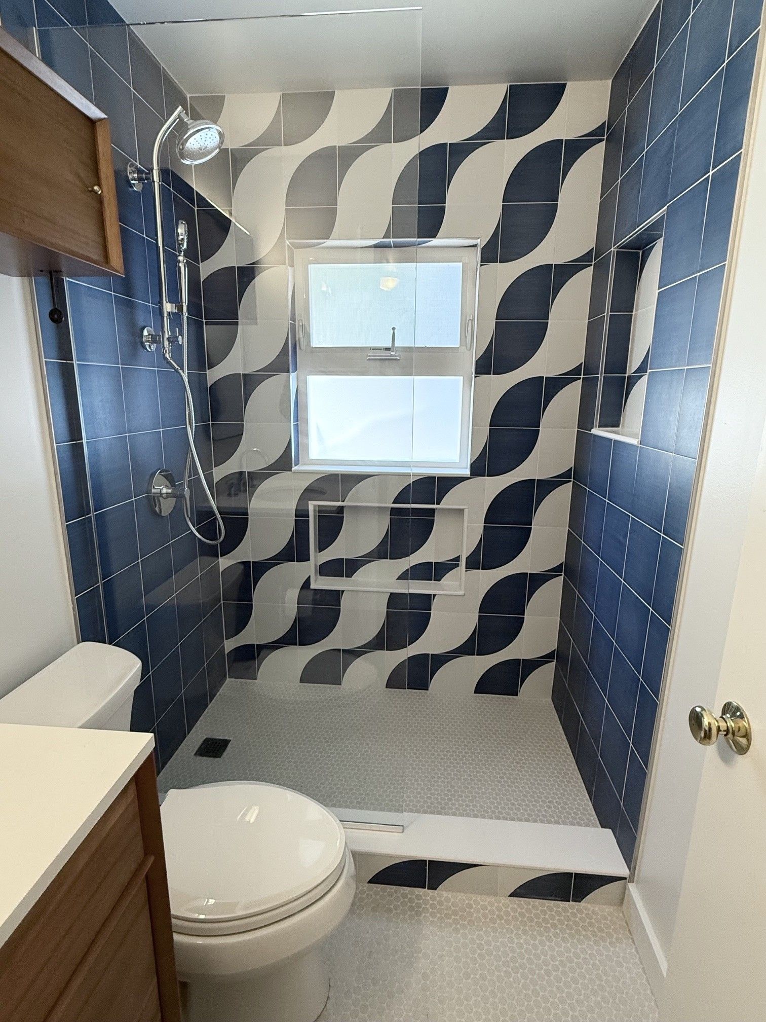 Small bathroom with black-and-white wavy tile shower, window, toilet, and sink cabinet