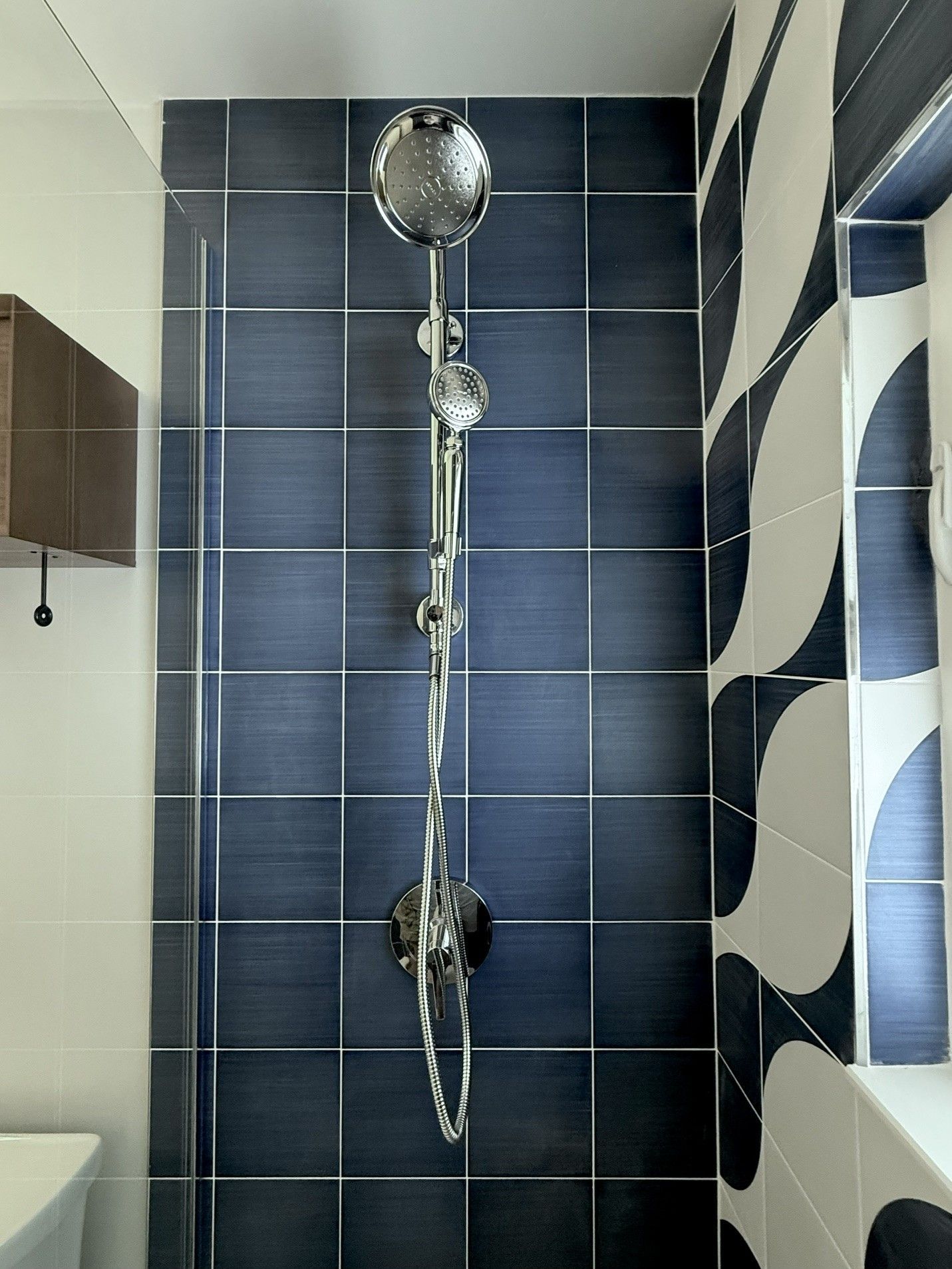 Blue-tiled shower with a chrome handheld showerhead and white-blue patterned curtain.