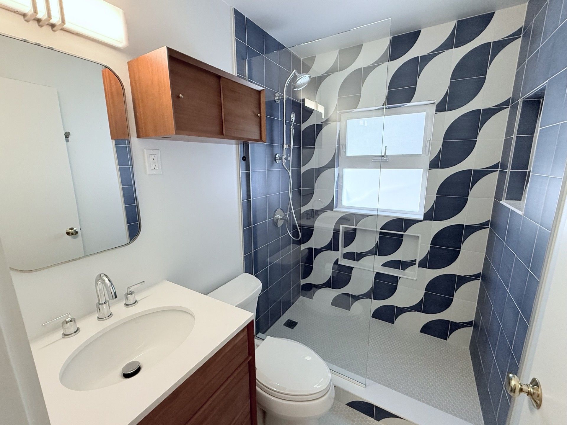 Small bathroom with white vanity, mirror, toilet, and a blue-and-white tiled shower