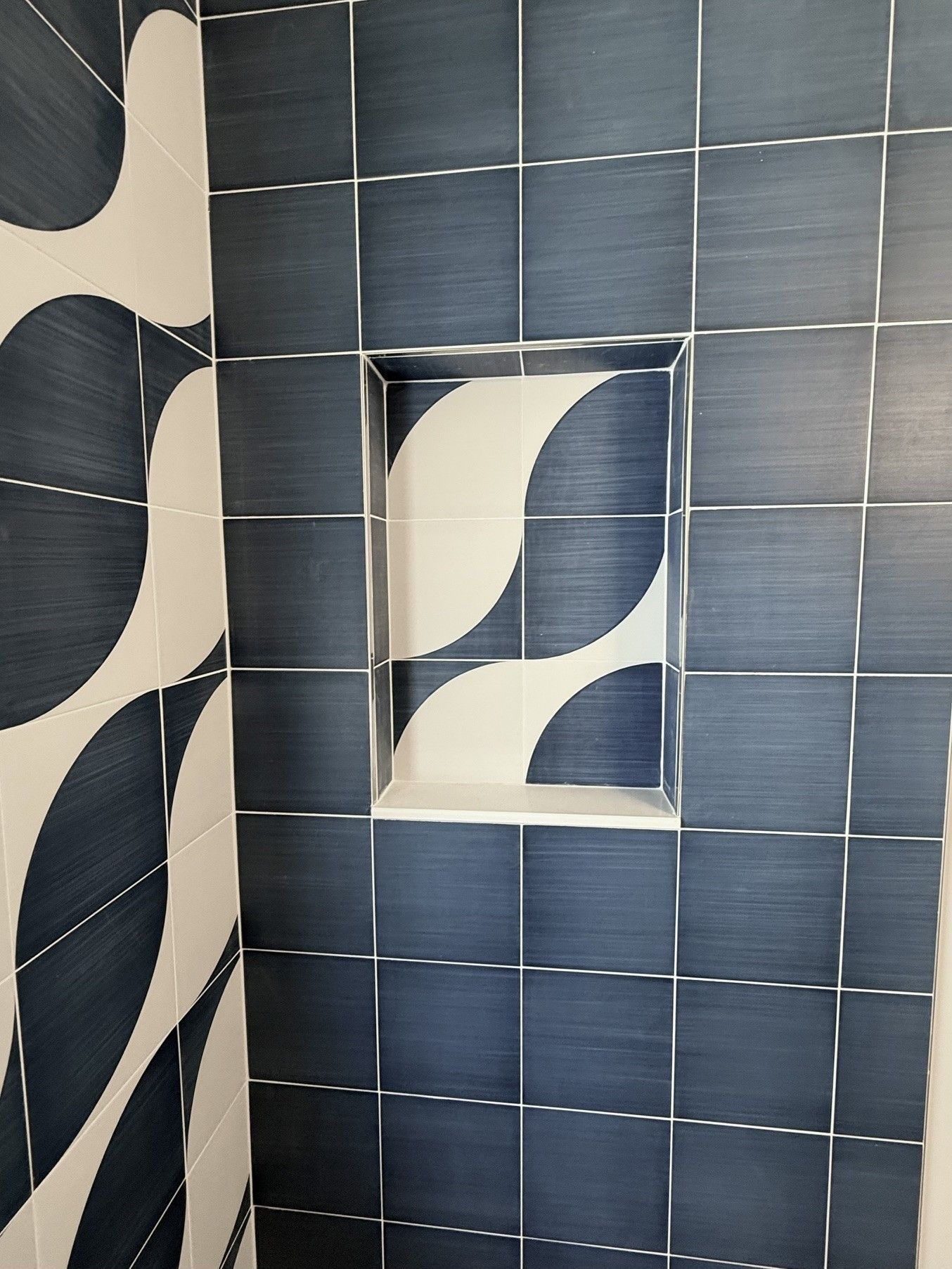 Blue tiled wall with a small inset featuring a black-and-cream abstract leaf pattern