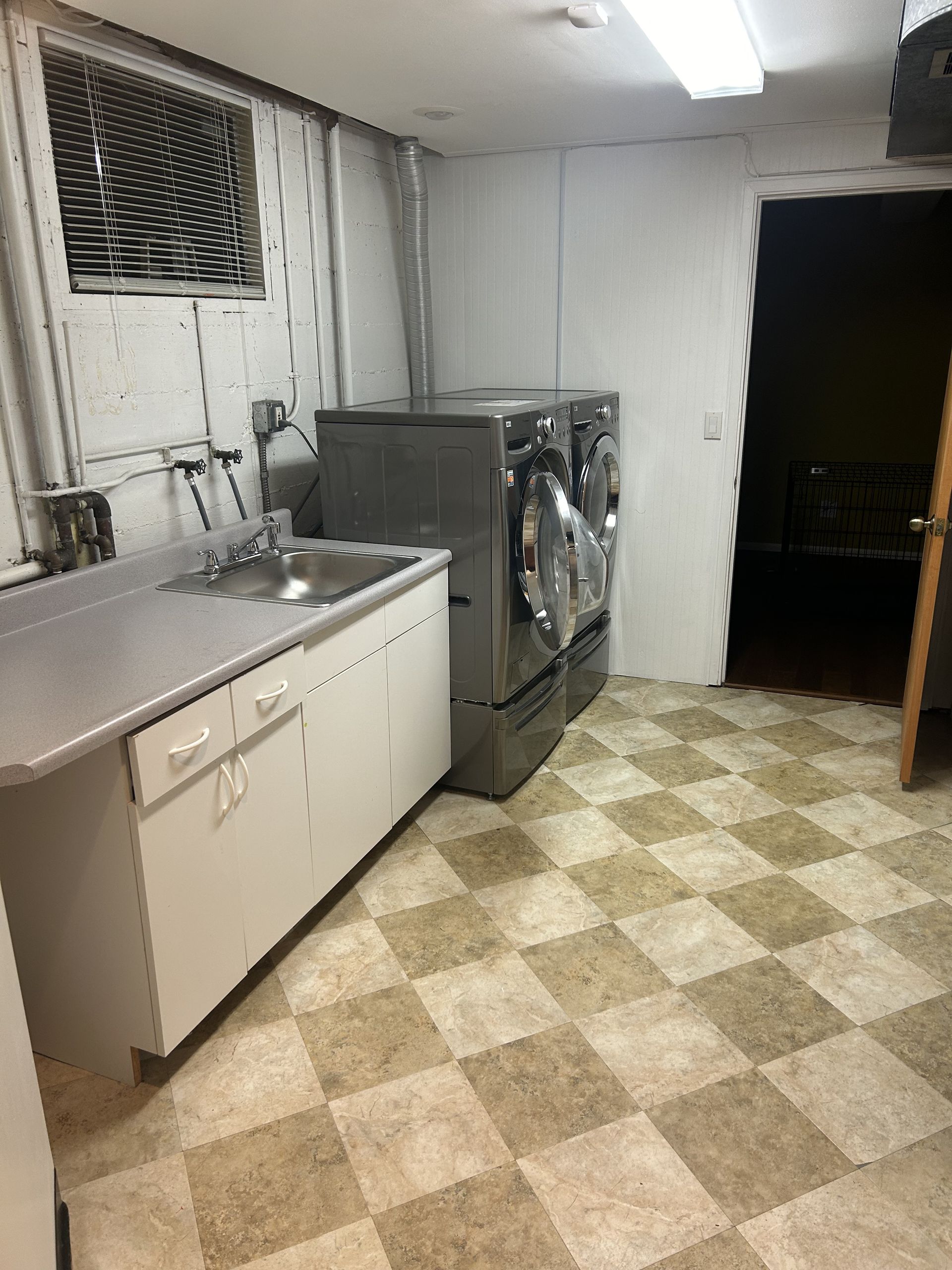 Small laundry room with sink, washer, white cabinets, and checkered tile floor.