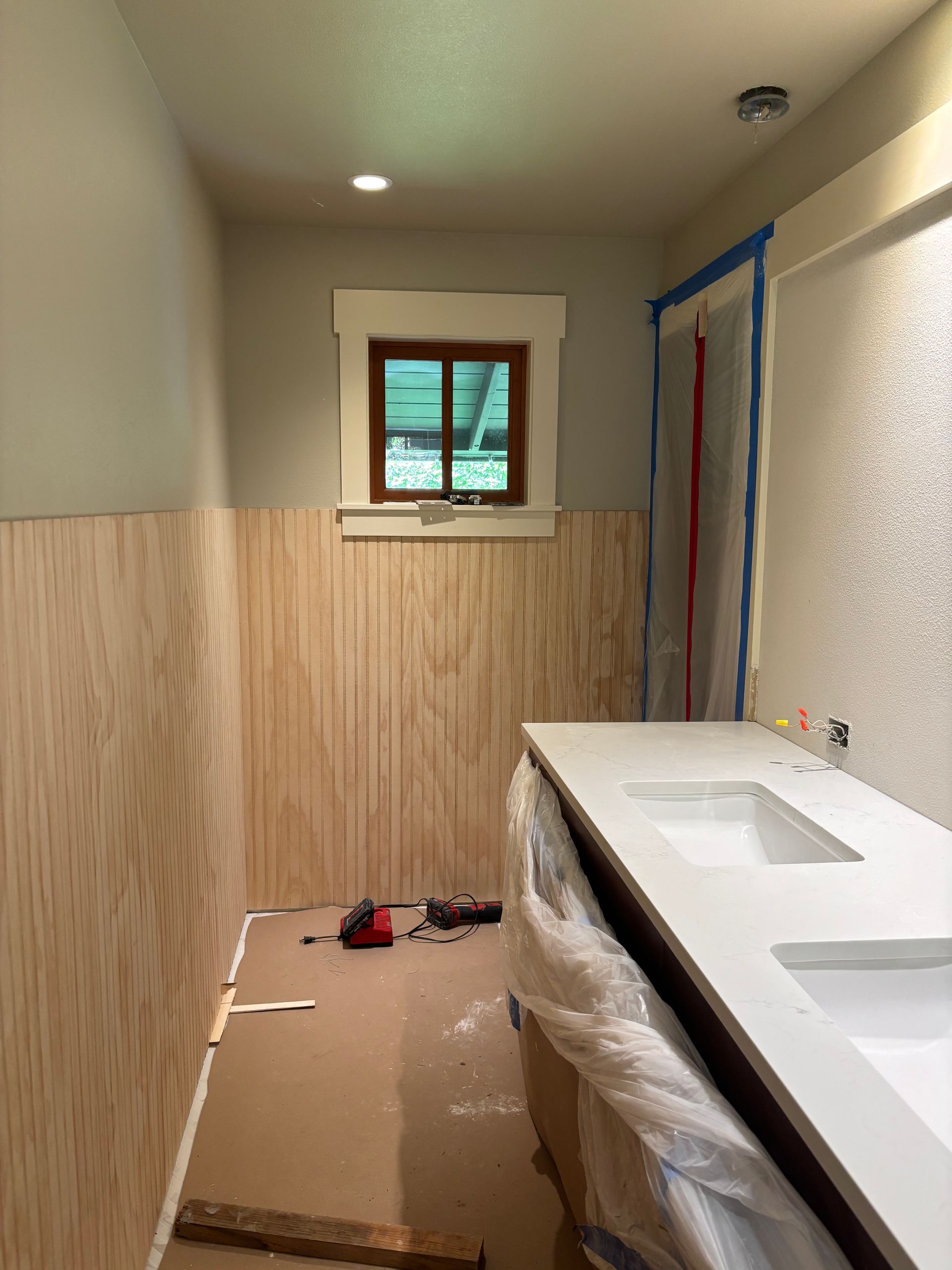 Narrow hallway under renovation with wainscoting, a window, and a sink or countertop covered in plastic.