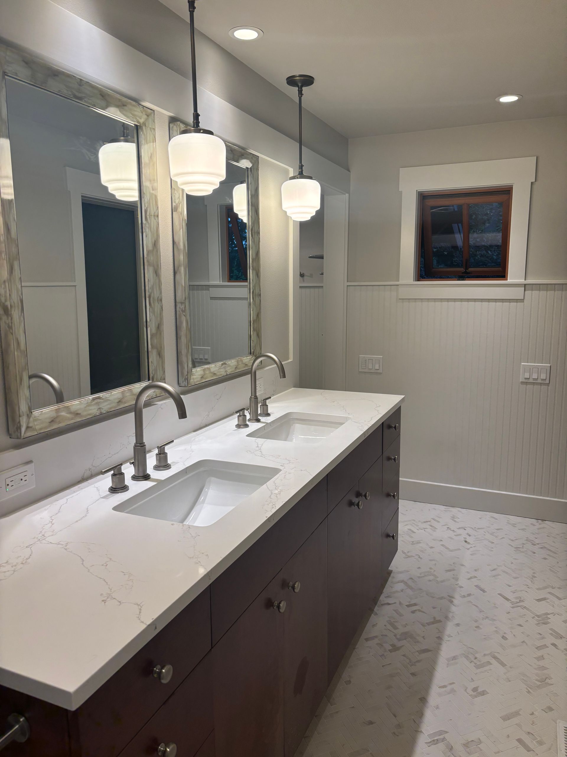 Bright bathroom with double vanity, large mirrors, pendant lights, and white tile floor.