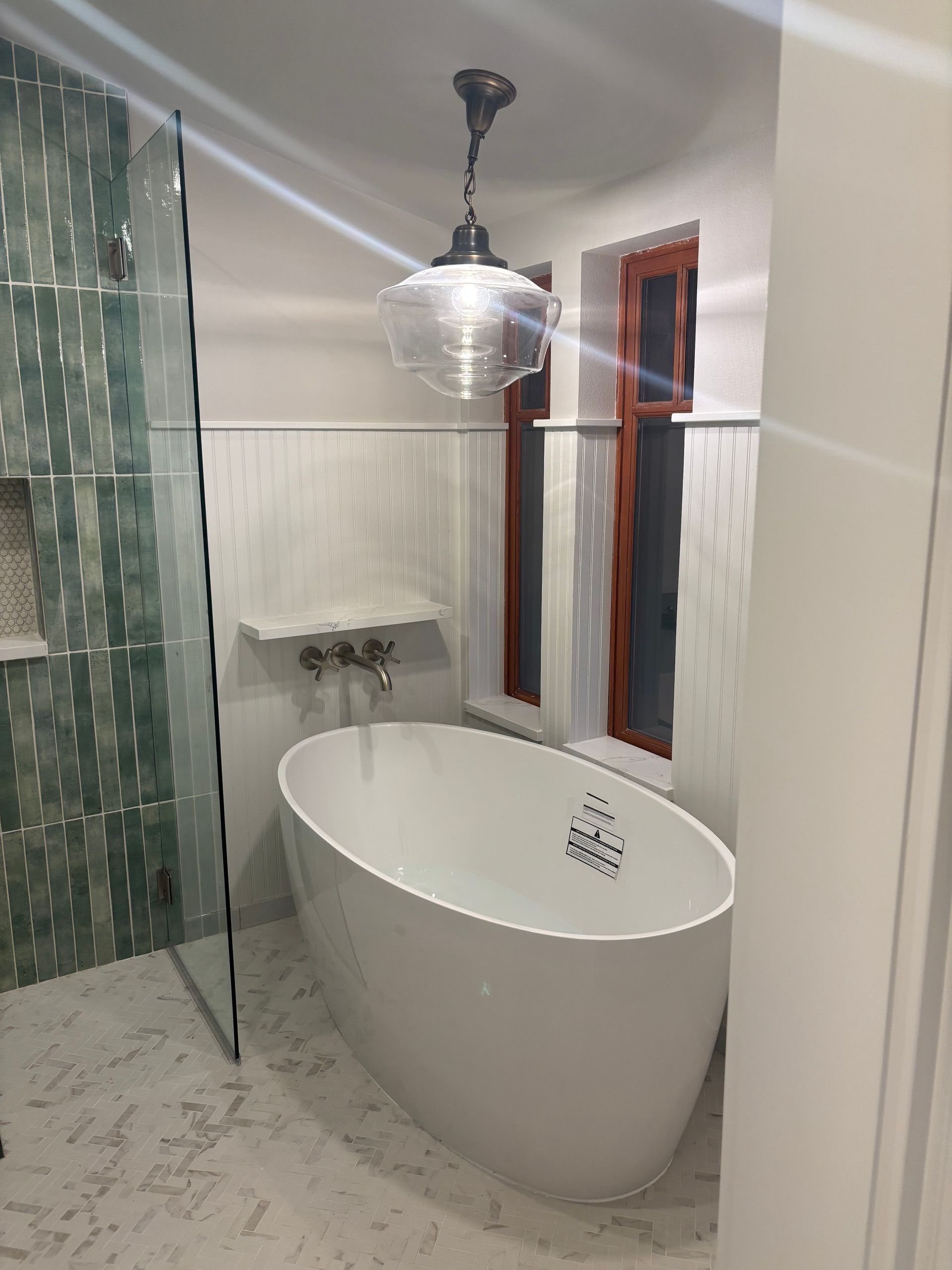 Modern bathroom with freestanding white tub, glass shower, sink, and pendant light