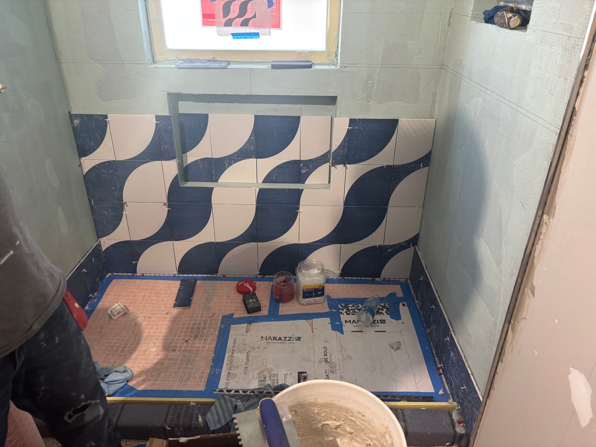 Bathroom under renovation with blue-and-white patterned wall tiles, tools, and a partially tiled floor.