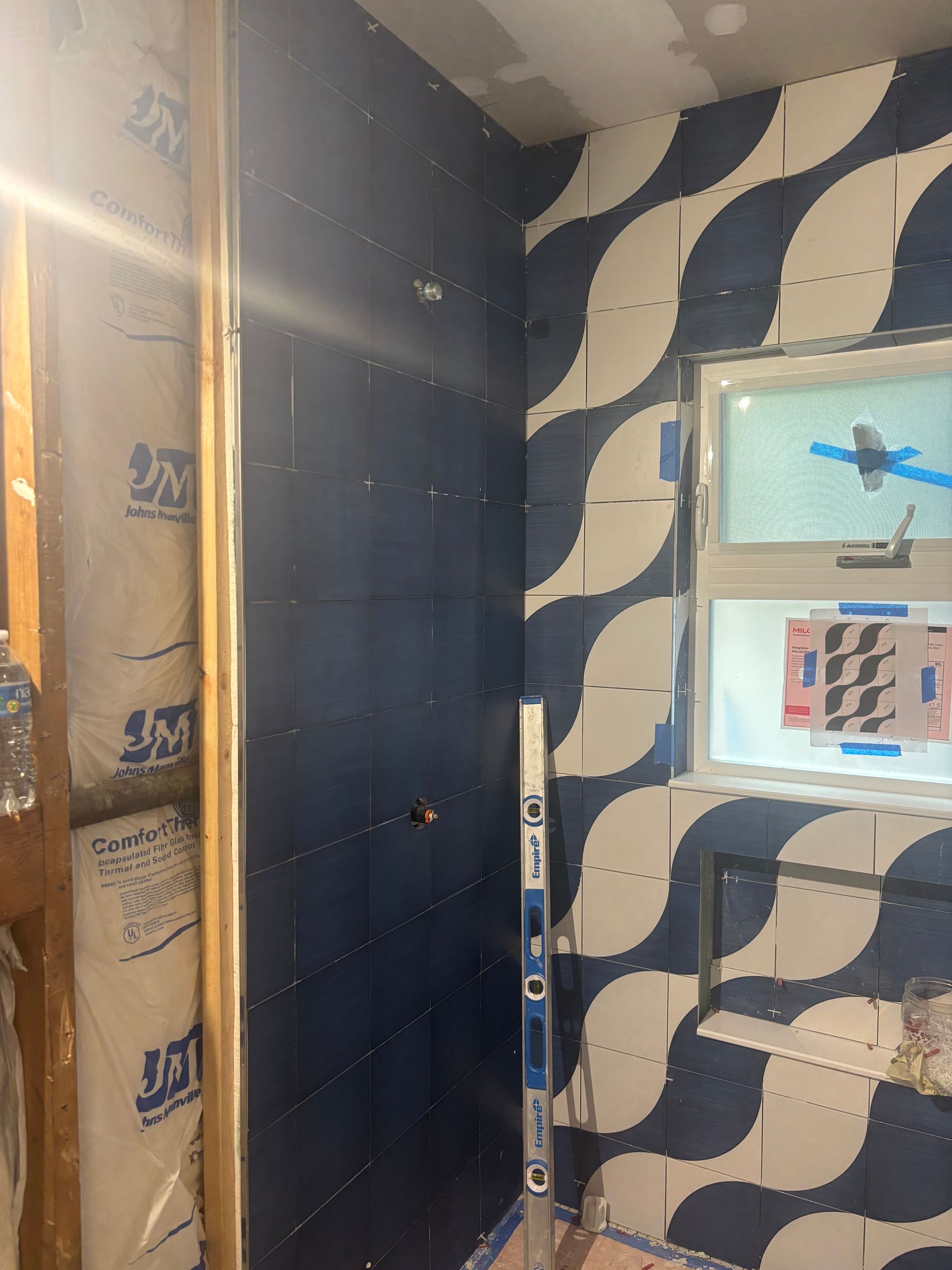 Interior wall under renovation with dark paneling, exposed insulation, and a patterned wallpaper section near a window.