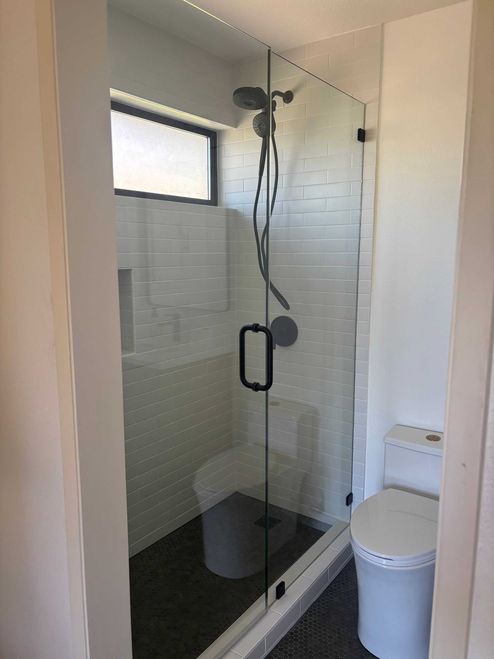 Small glass shower with black fixtures, white tile, and a toilet beside it in a compact bathroom