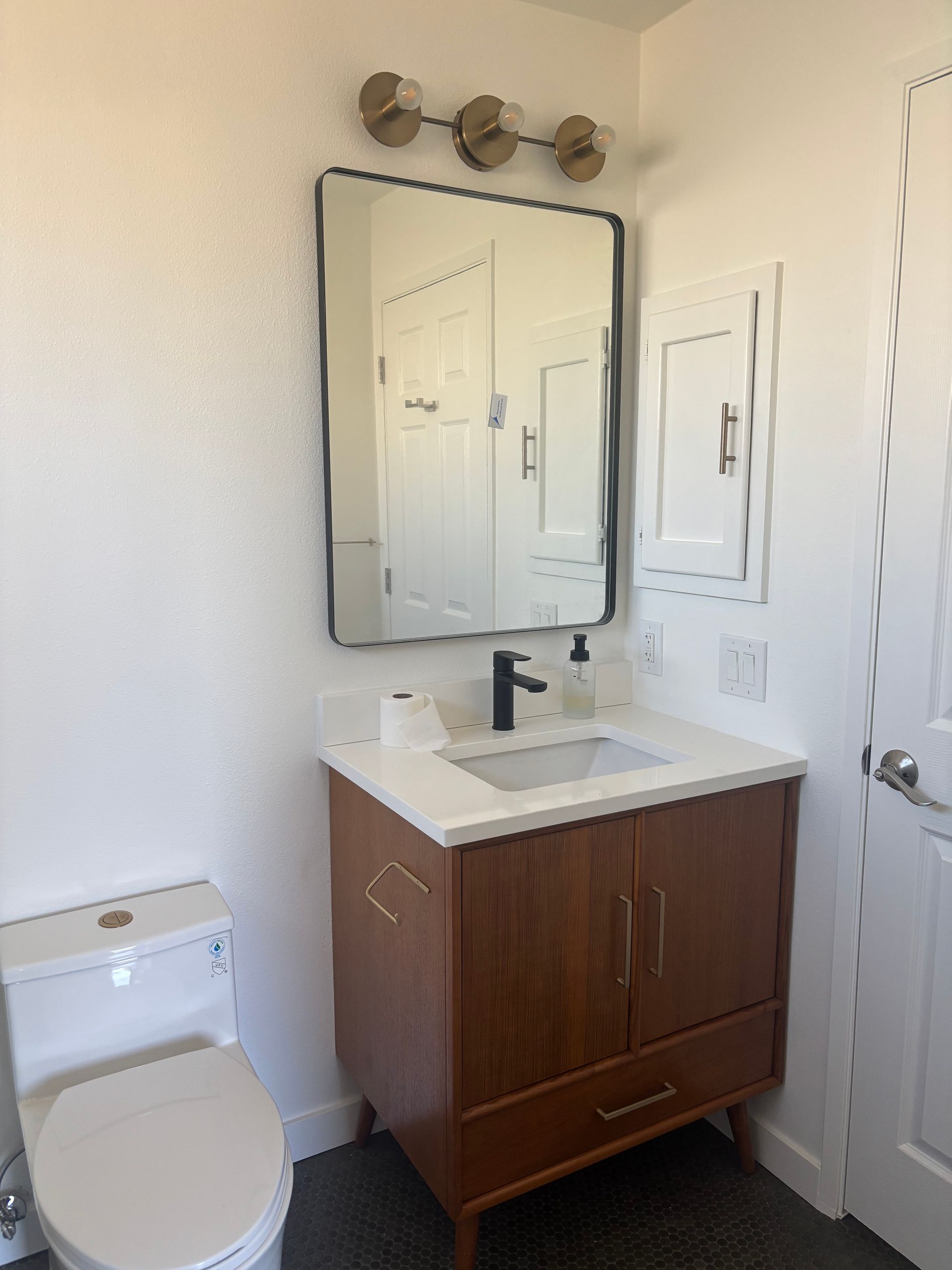 Small bathroom with white toilet, wood vanity, mirror, sink, and a closed door.
