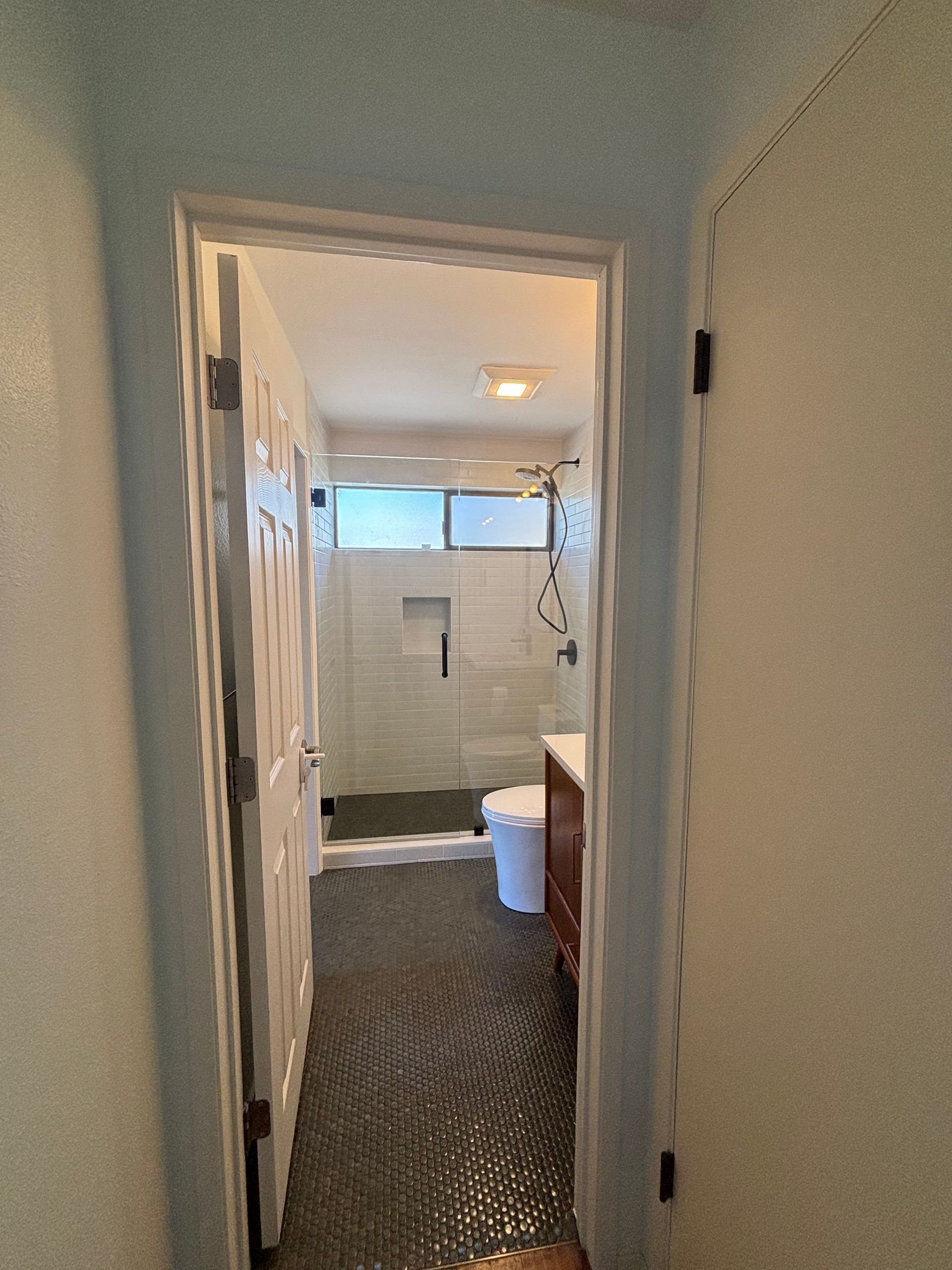 Narrow bathroom hallway with an open doorway, tiled floor, window, and a vanity visible inside.