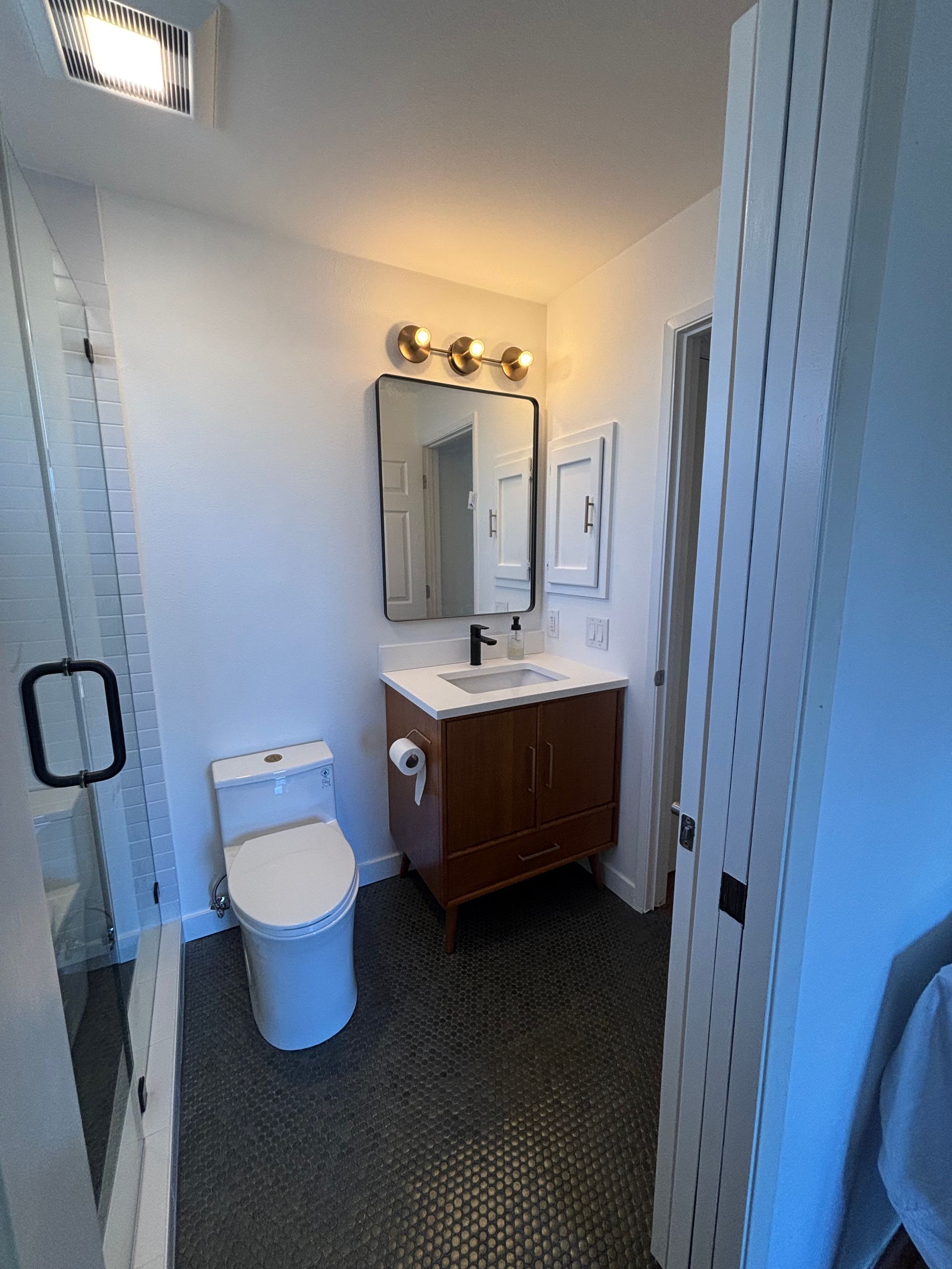 Small bathroom with toilet, vanity sink, mirror, and shower curtain in a narrow white room.