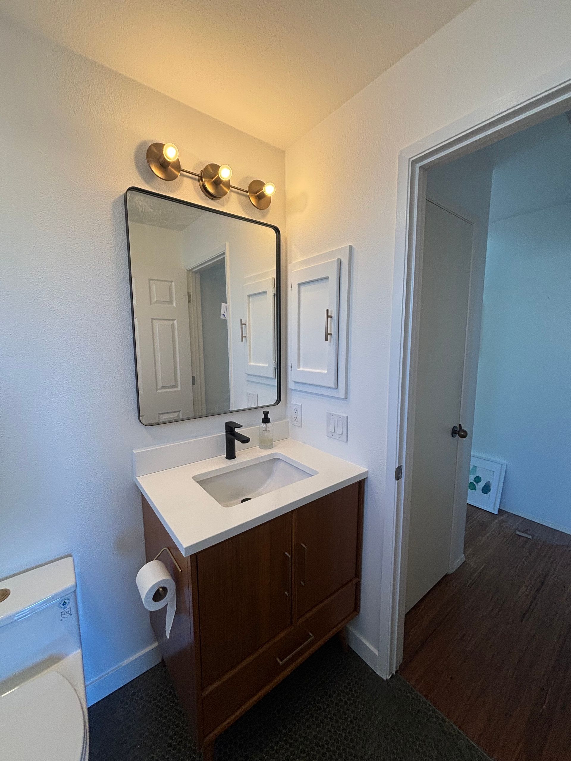 Small bathroom vanity with mirror, lights, sink, and open door to a hallway or adjacent room.