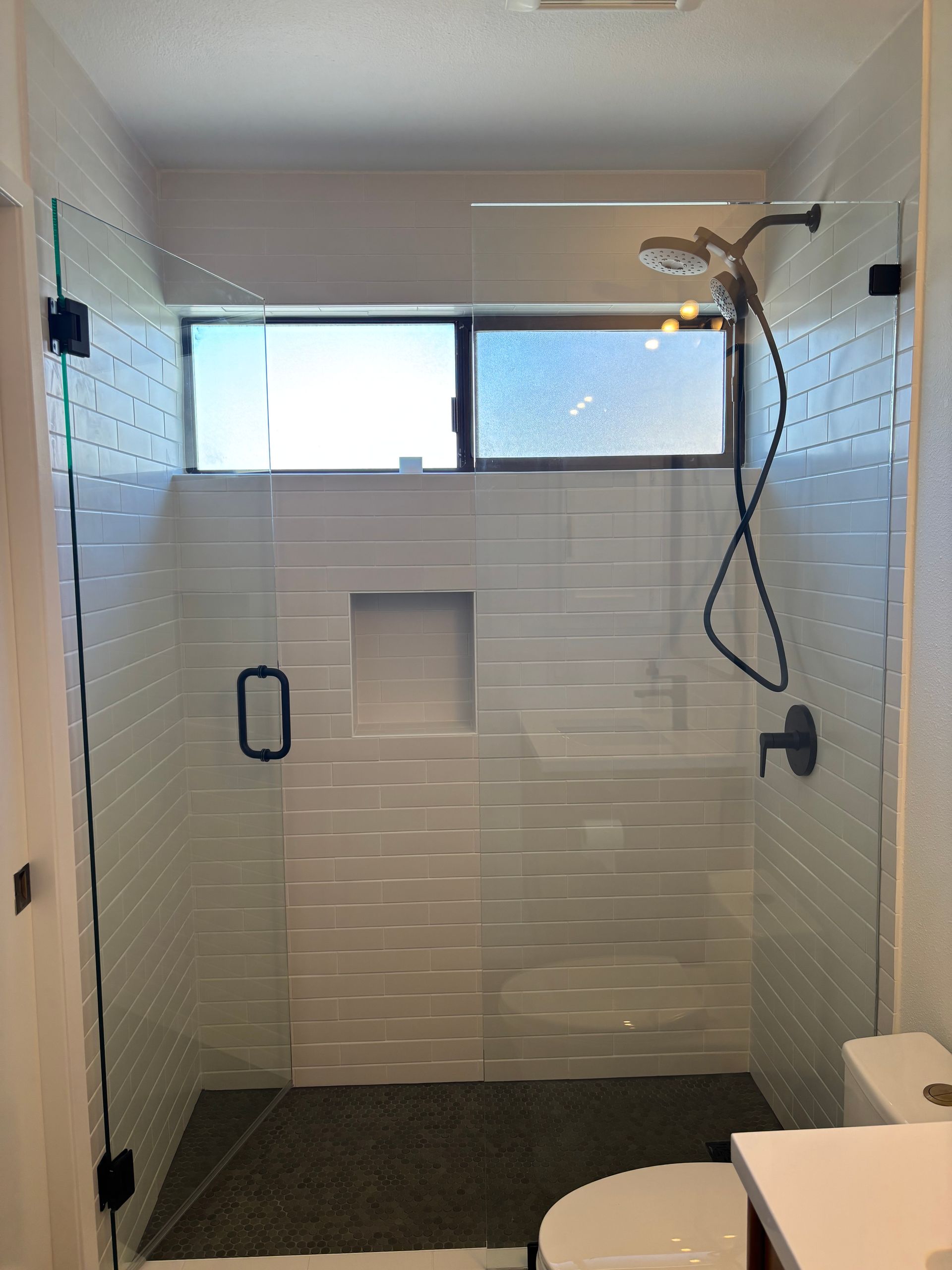 Walk-in shower with white tile walls, bench niche, black grab bar, and handheld showerhead