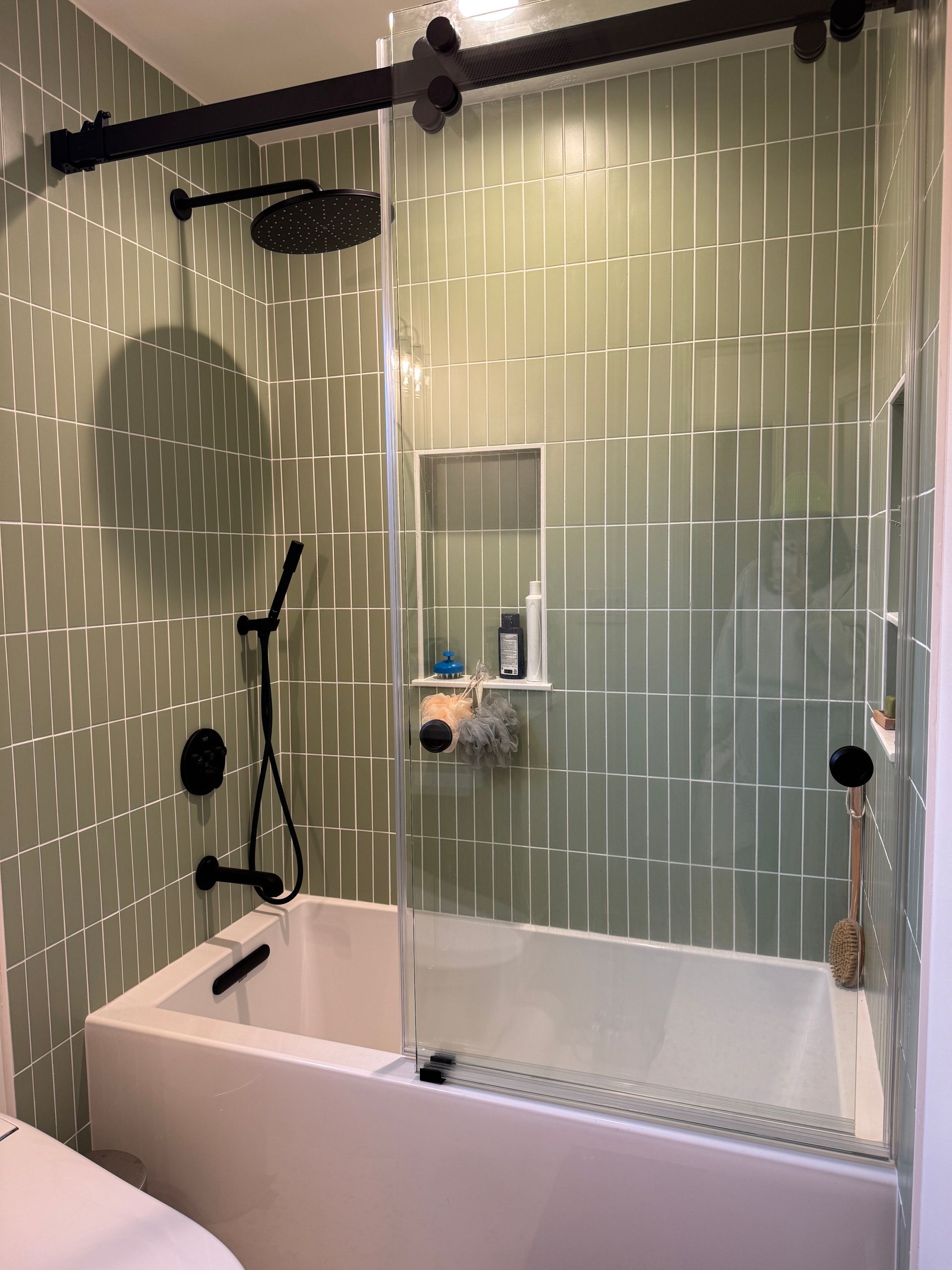 Modern bathroom with white tiled walk-in shower, glass panel, black showerhead, and bathtub combo
