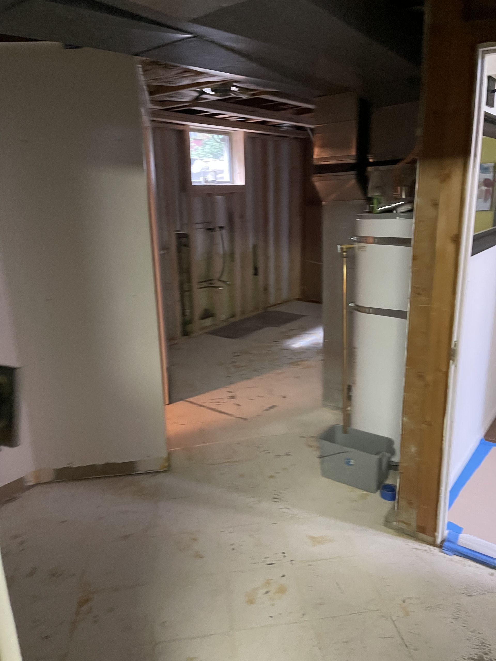 Dim unfinished basement hallway with exposed studs, small window, and a water heater.