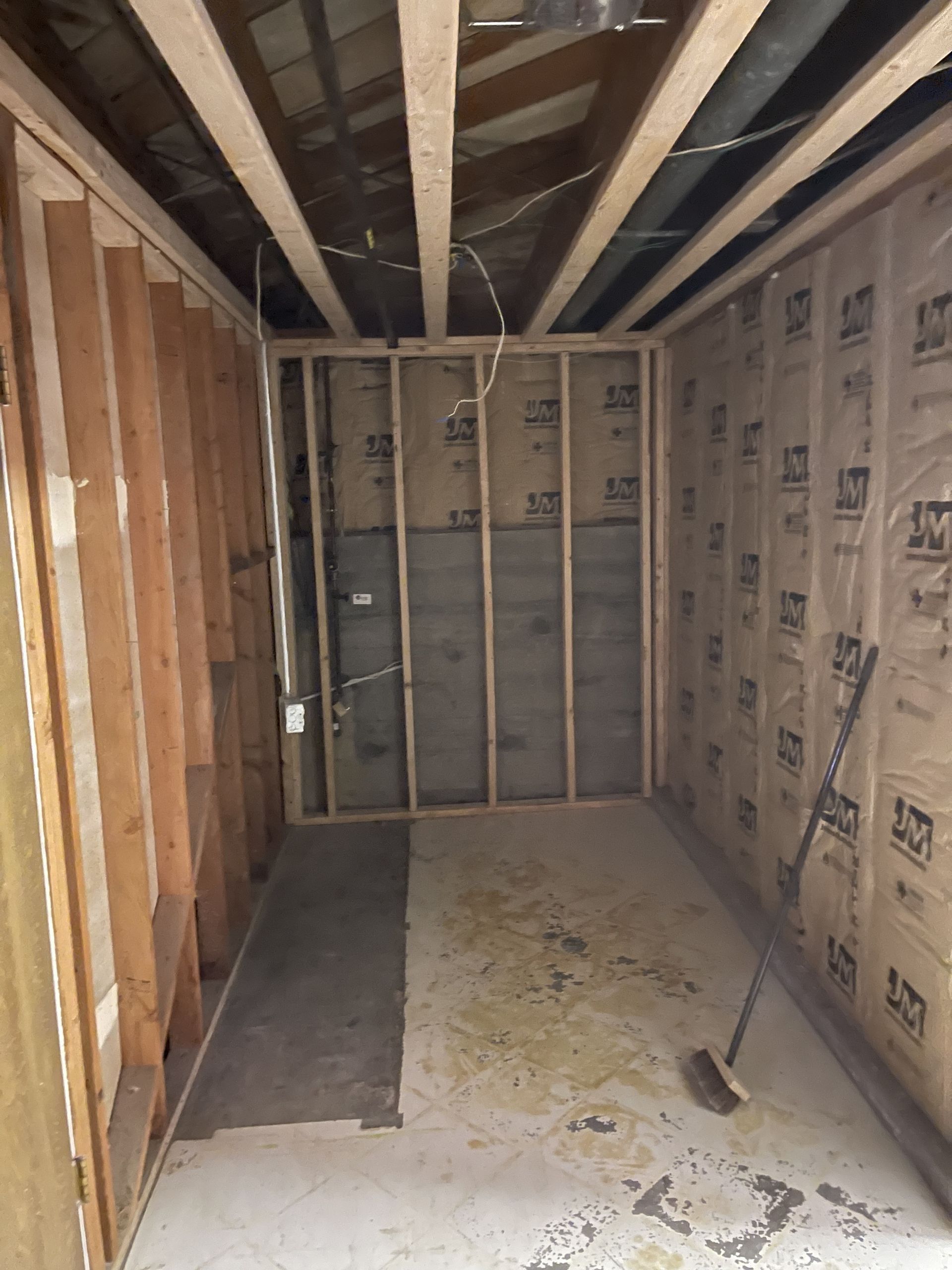 Unfinished basement room with exposed framing, insulation, and concrete floor under low joists.