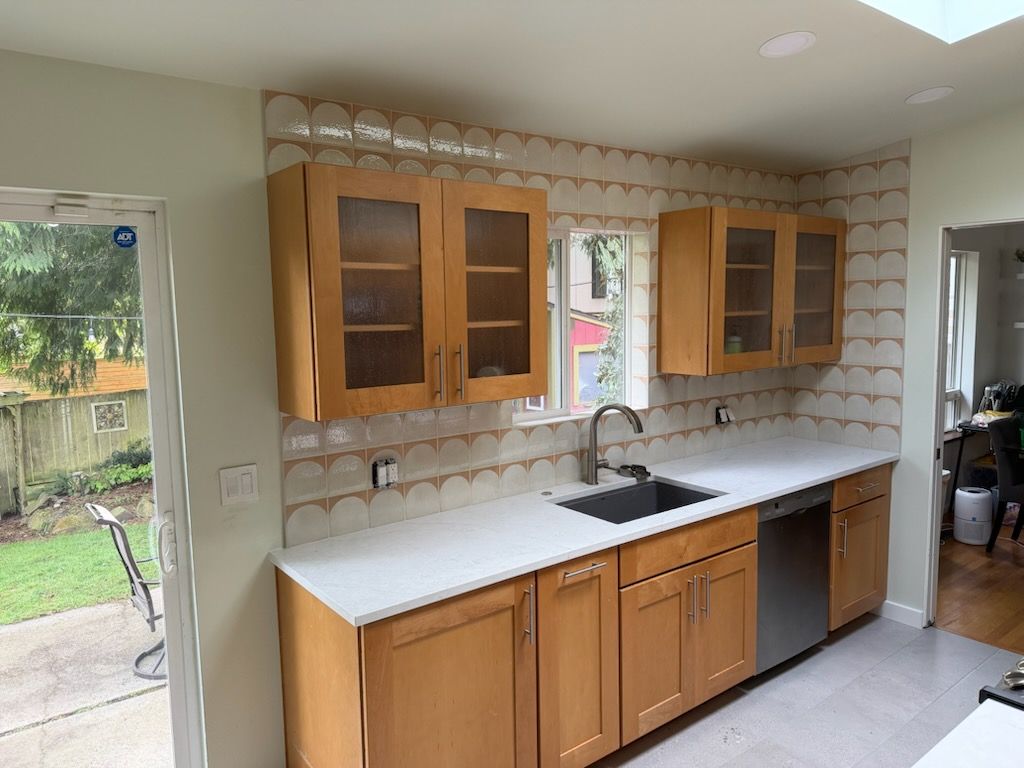 Kitchen with wood cabinets, white countertops, tiled backsplash, and a sink by a sliding glass door.
