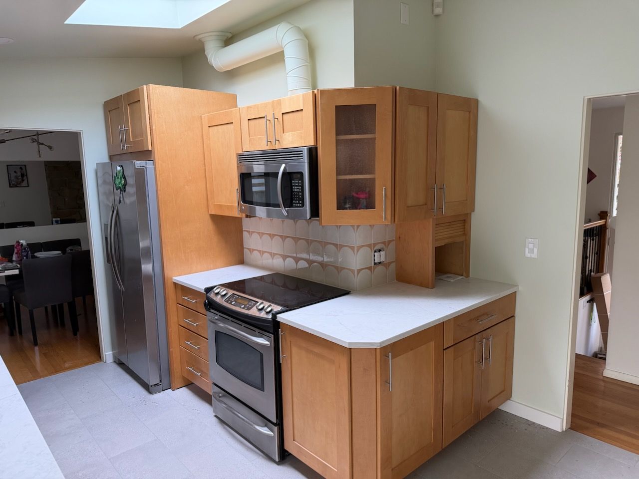 Small kitchen with wood cabinets, stainless steel fridge and stove, white countertops, and a tiled backsplash.