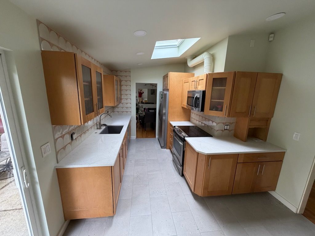 Long, narrow kitchen with wood cabinets, white counters, and skylight, viewed from the doorway