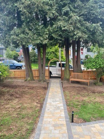 Tree-lined walkway leading to a white pickup truck, with benches and shrubs in a small park.