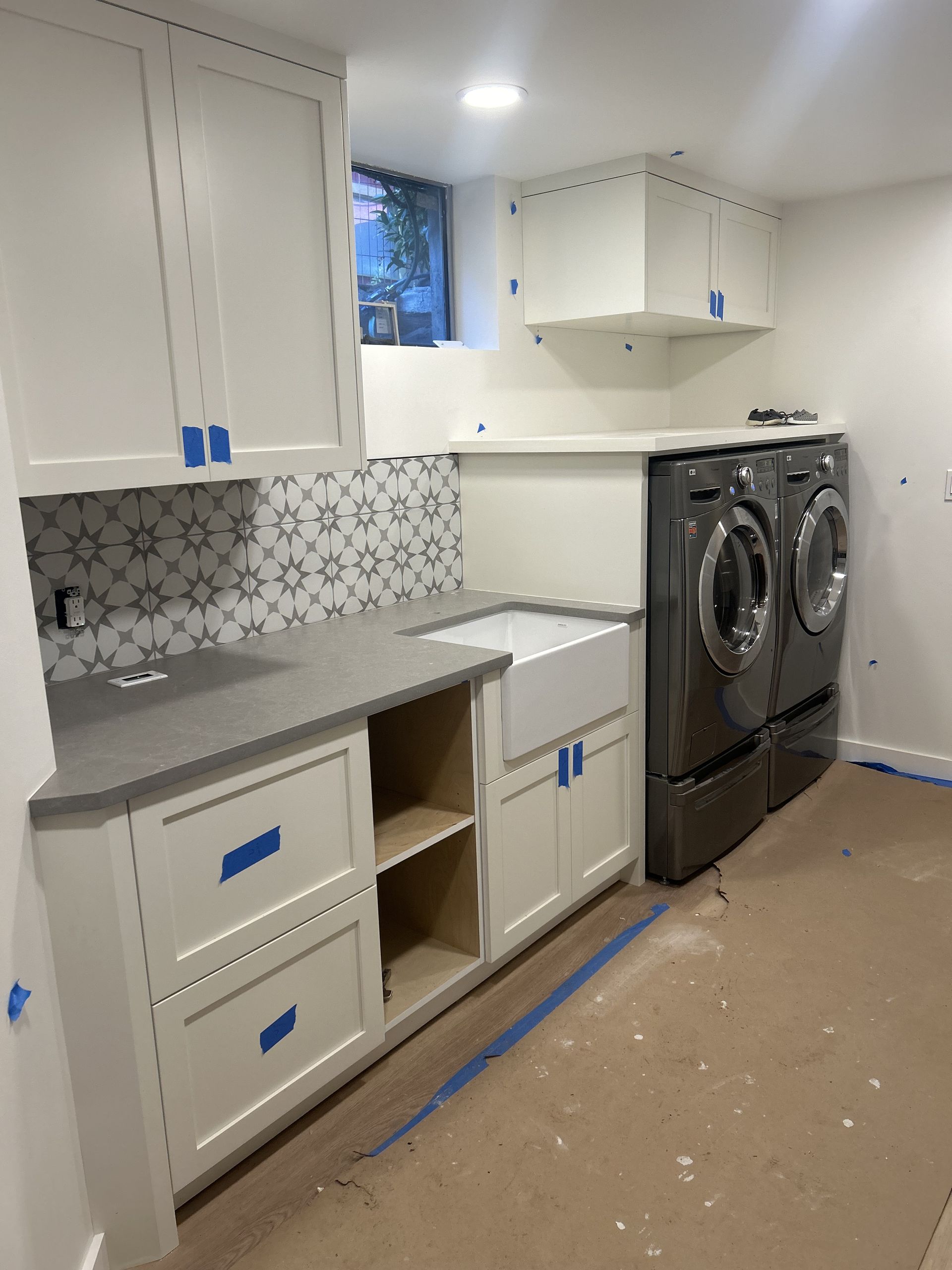 Unfinished kitchen with white cabinets, gray countertop, patterned backsplash, and stacked washer and dryer.