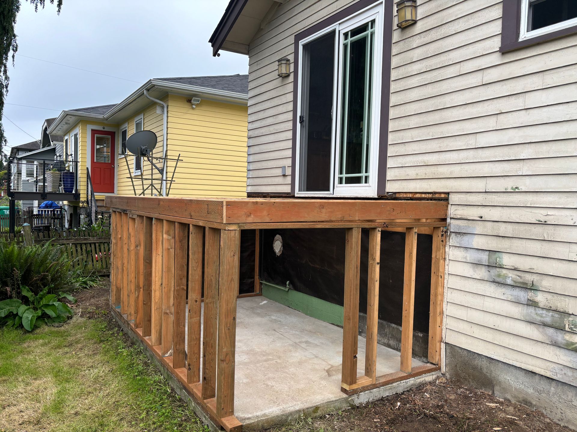 Wooden accessibility ramp beside a beige house, leading to a doorway in a residential yard.