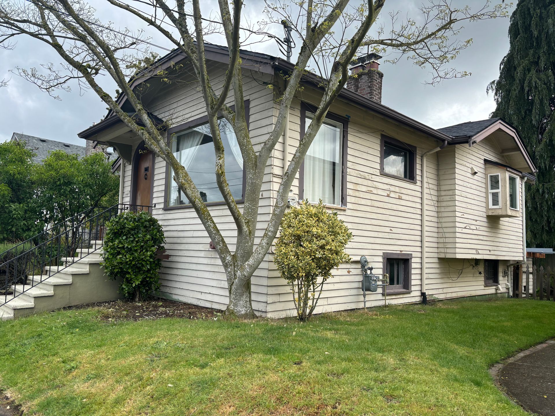 Two-story cream house with dark roof, front stairs, and leafless trees on a green lawn