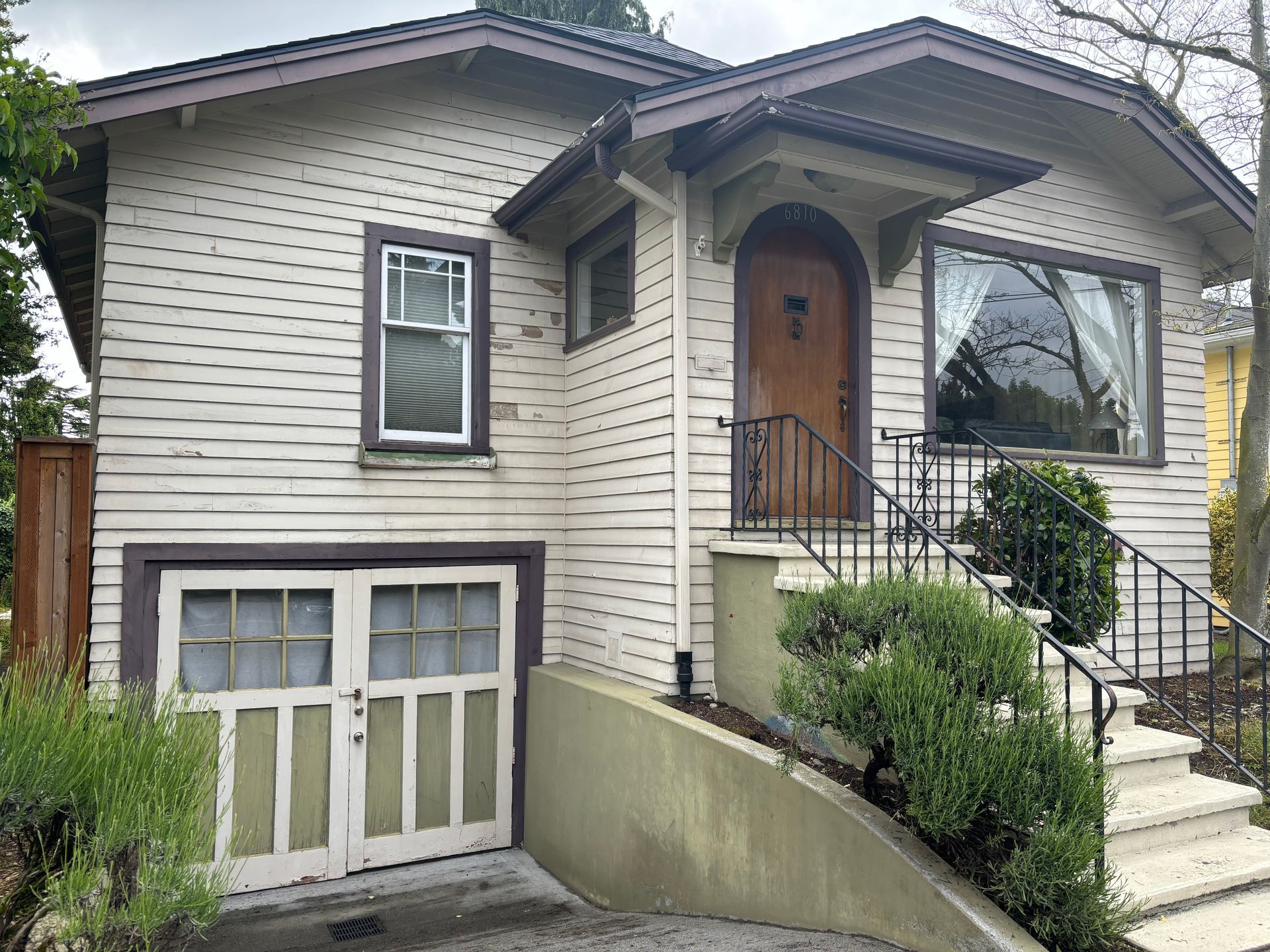 Small beige house with a front porch, steps, and a garage door under the main level.