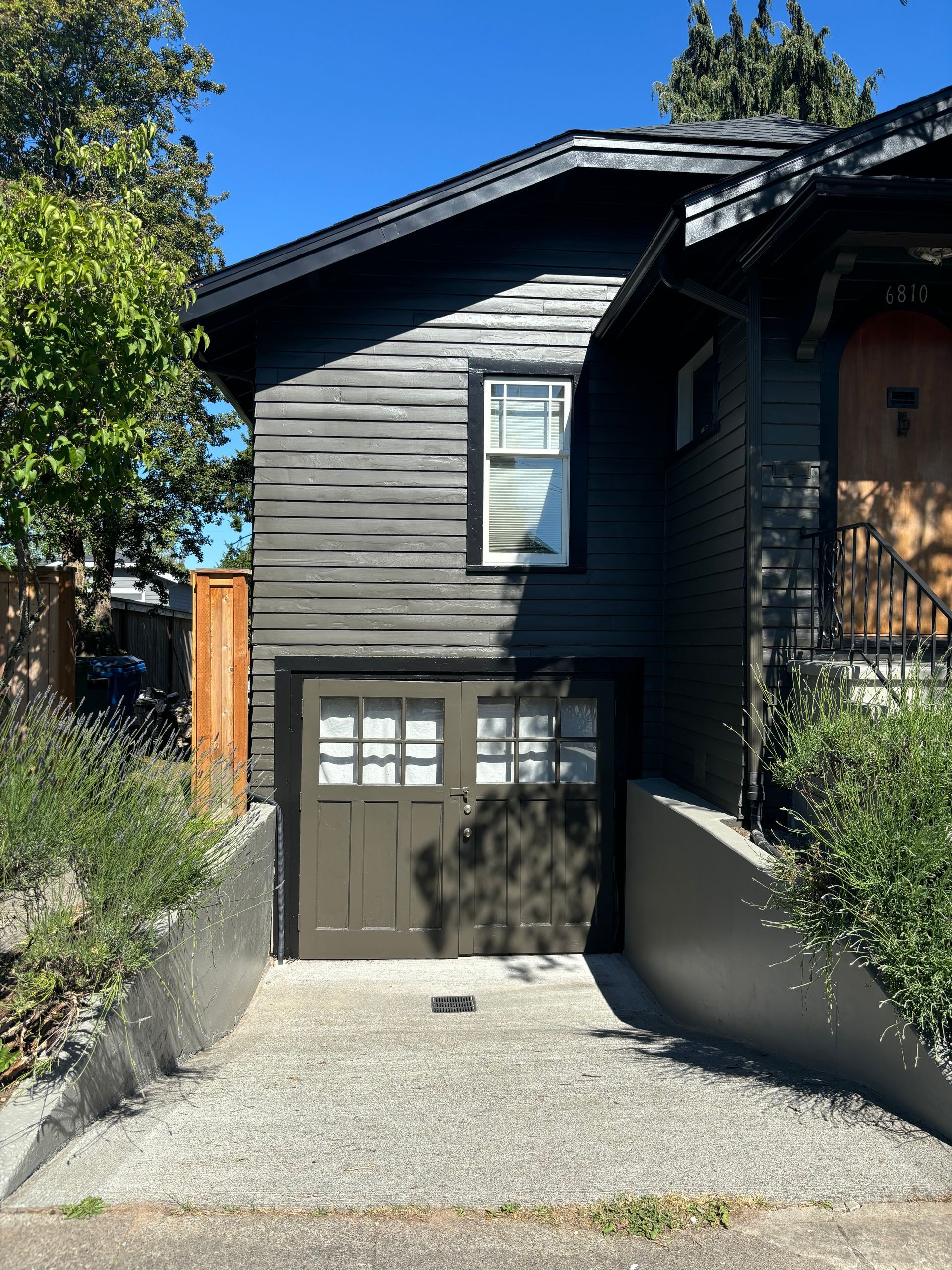 Dark gray house with garage door and upper window, viewed from a driveway between low walls.