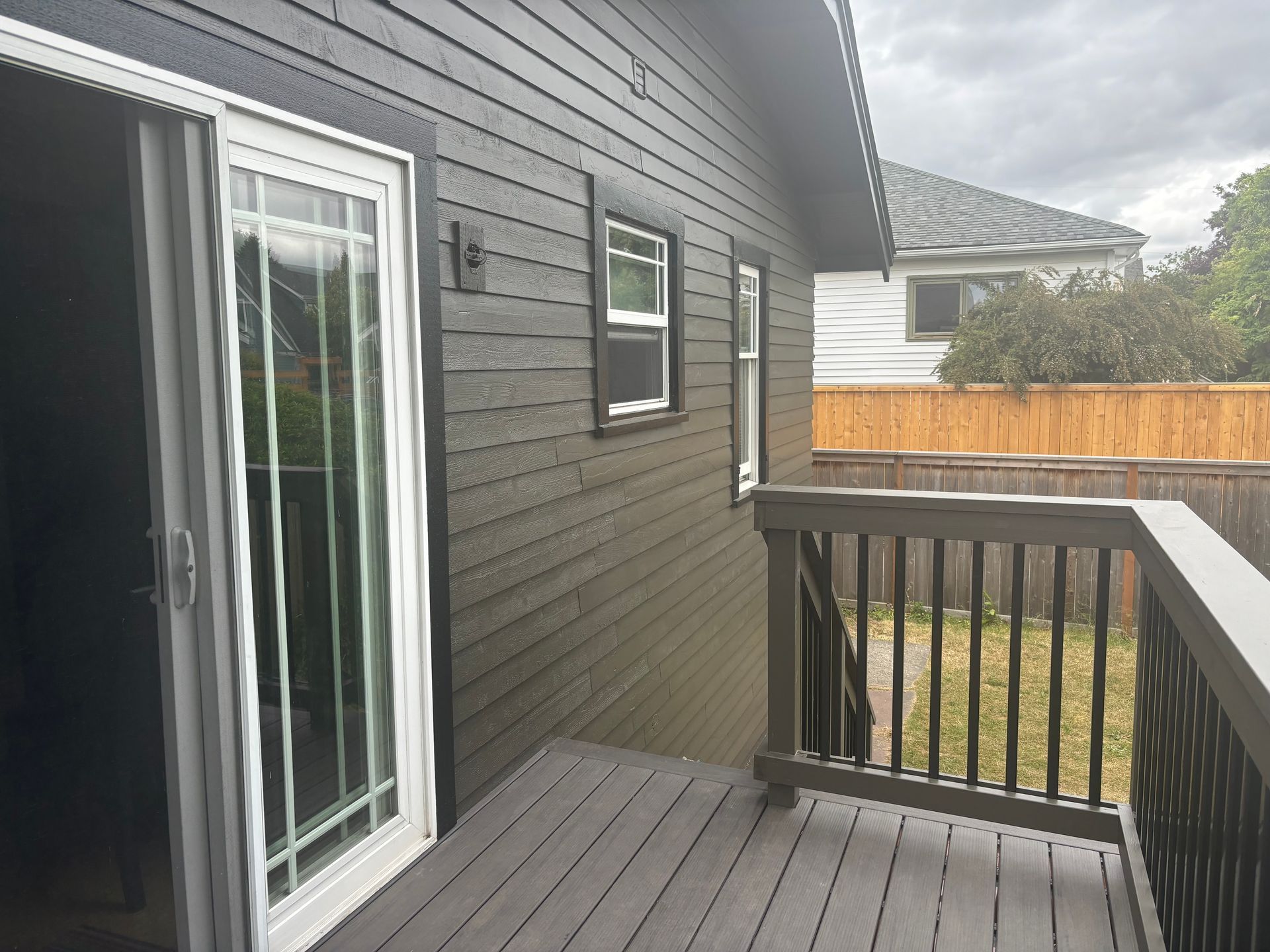 Gray house deck with black railing, sliding glass door, and fenced backyard view